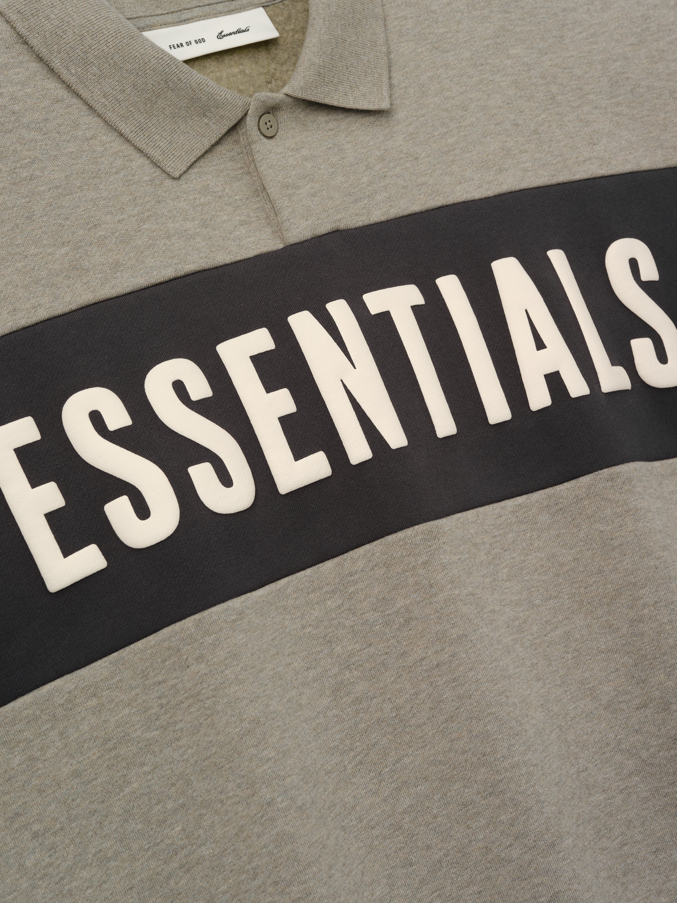 Kids Cropped Polo in a muted grey shade with a contrasting dark horizontal panel featuring raised "ESSENTIALS" lettering, designed as a trendy and comfortable kids top.