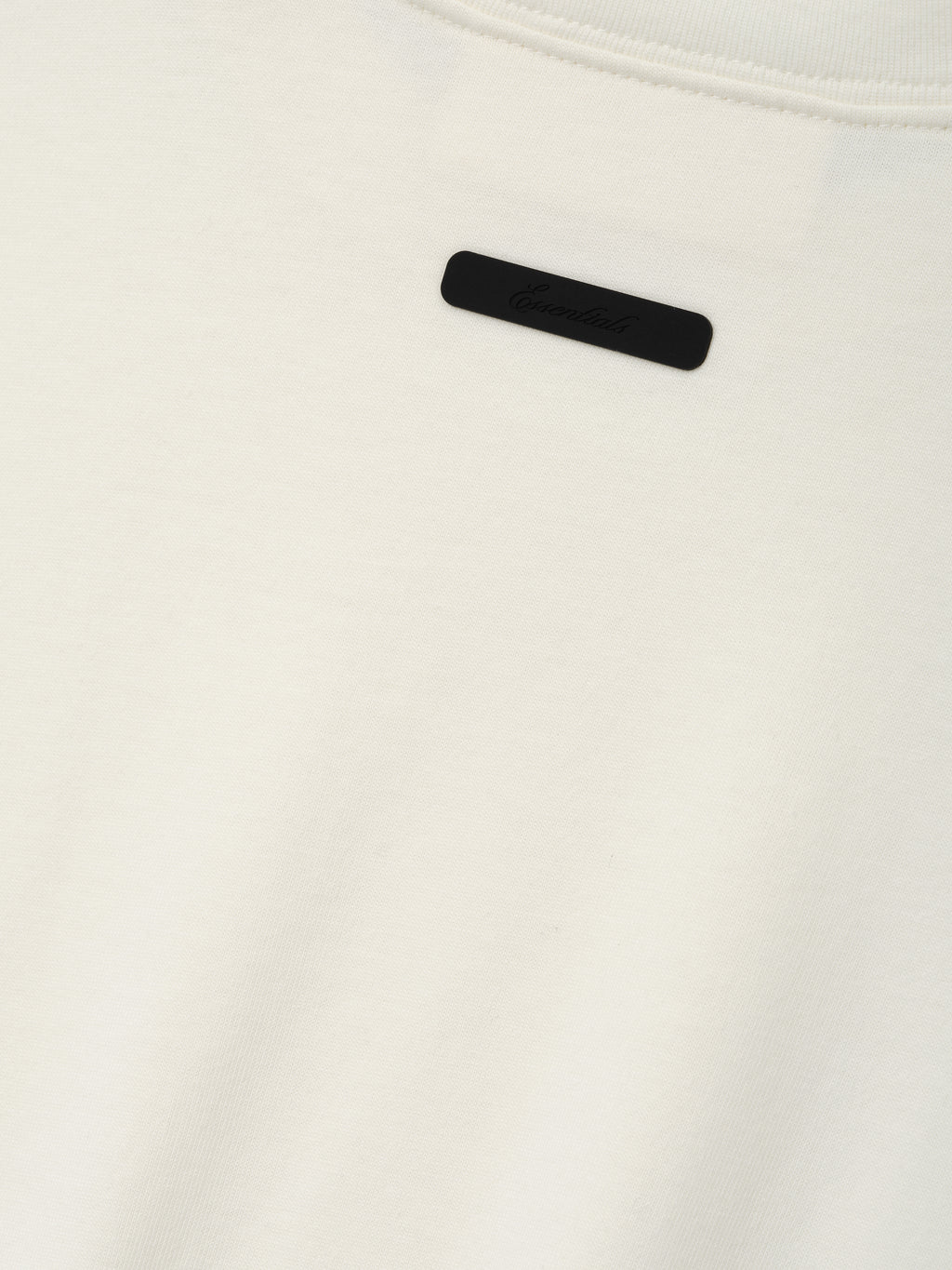 Kids Tri-Blend Essential Tee in a soft ivory fabric featuring a subtle black rectangular logo tag sewn near the neckline for a minimalist, stylish touch.