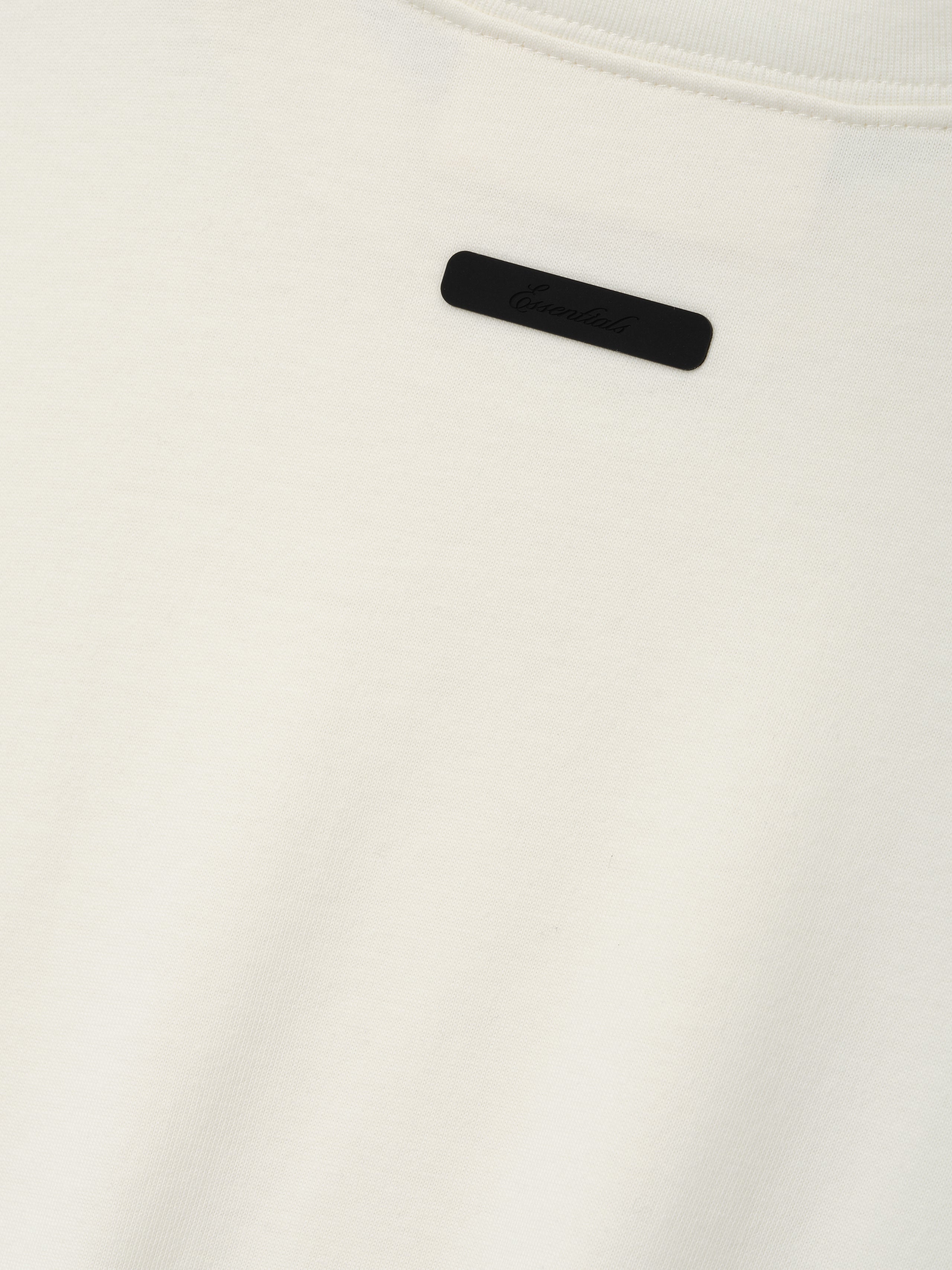 Kids Tri-Blend Essential Tee in a soft ivory fabric featuring a subtle black rectangular logo tag sewn near the neckline for a minimalist, stylish touch.
