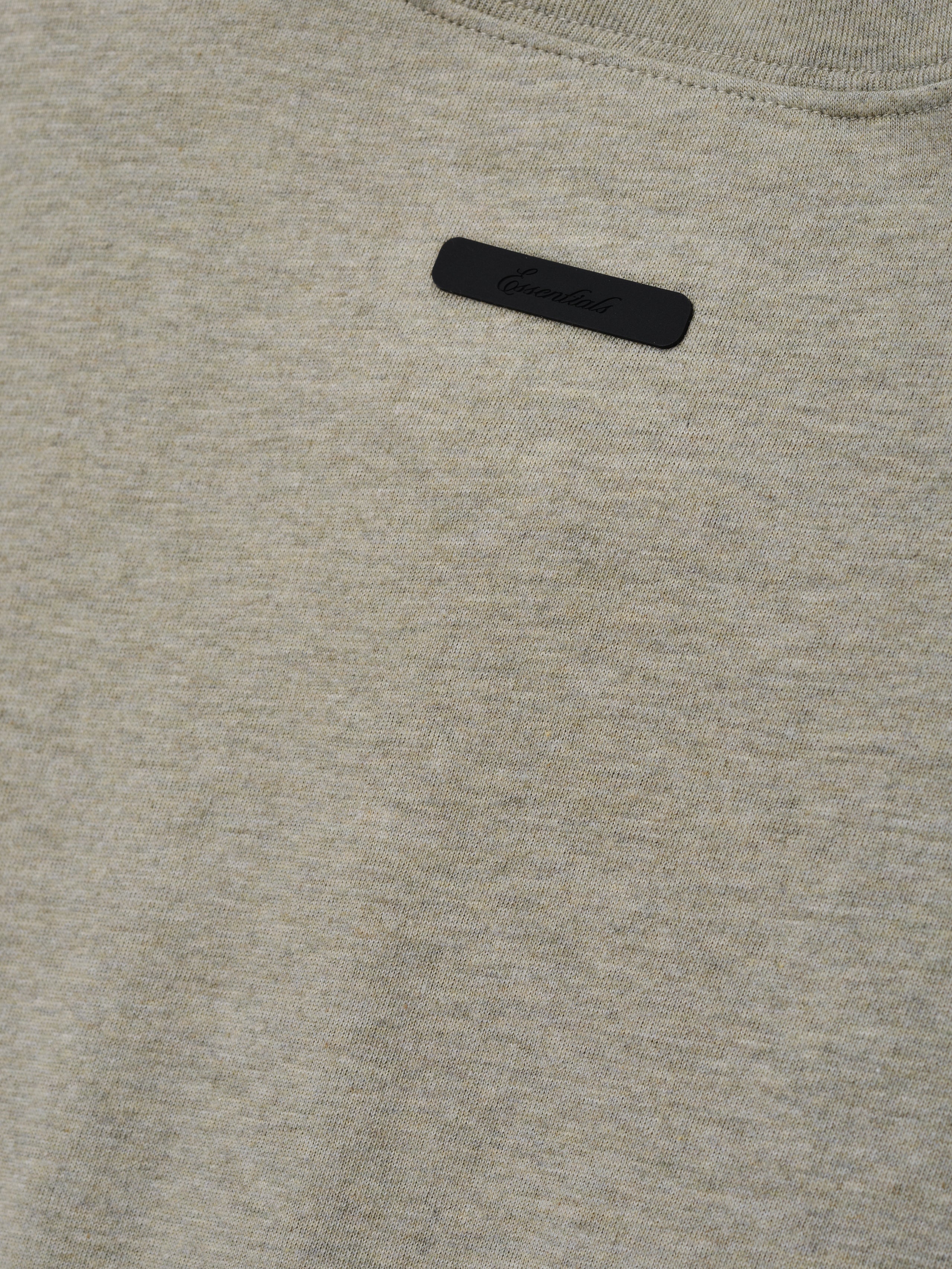Kids Tri-Blend Essential Tee in a muted beige heather fabric featuring a small black rectangular label with subtle embossed branding near the neckline for a clean, modern look.
