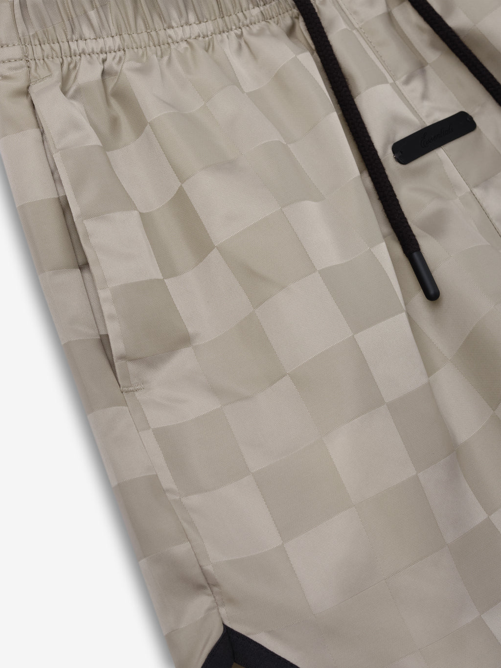 Kids Gym Short in a soft beige tone with an elastic waistband and subtle checkered pattern, featuring black drawstrings and a sleek label detail for a casual sporty style.