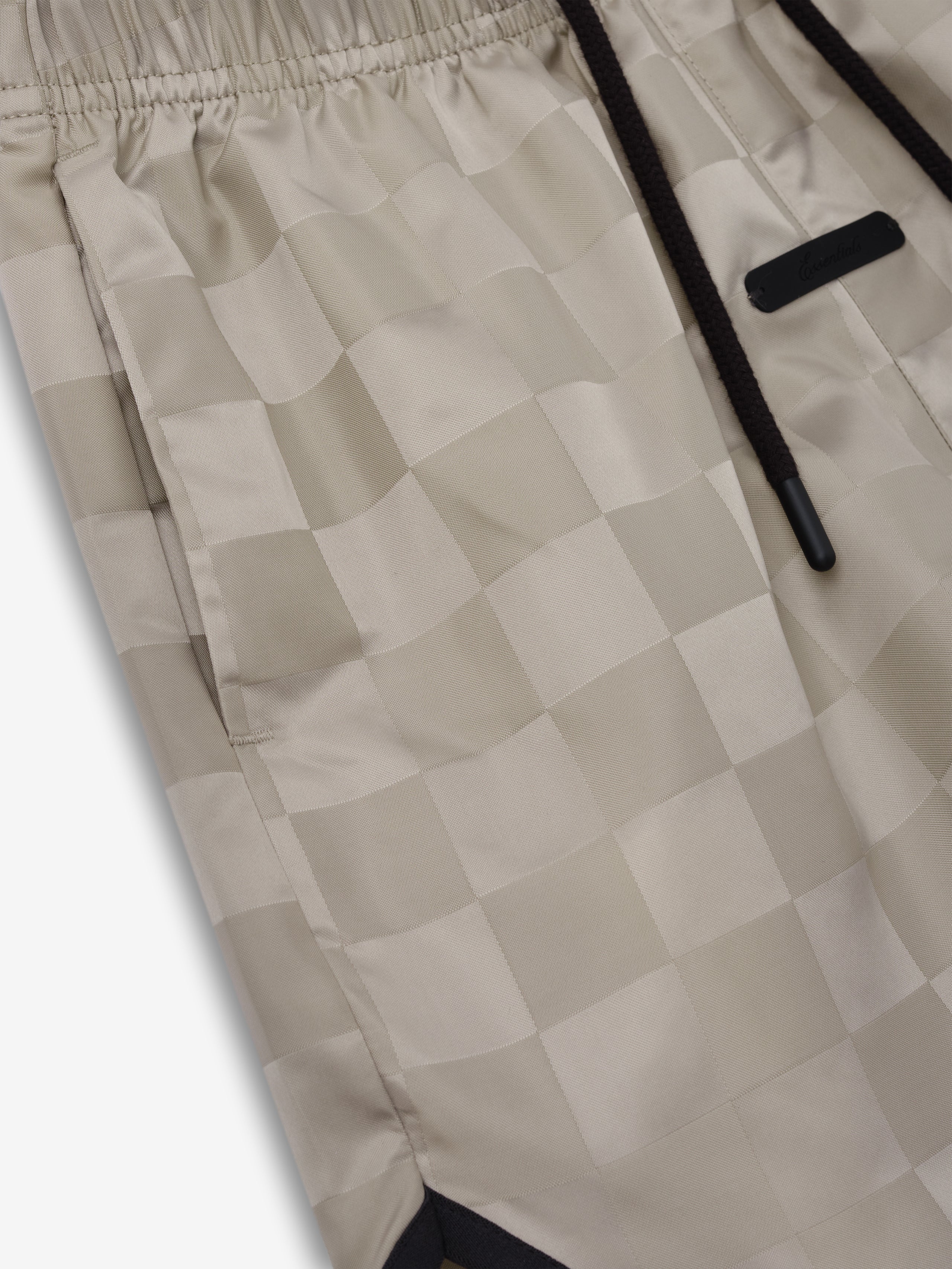 Kids Gym Short in a soft beige tone with an elastic waistband and subtle checkered pattern, featuring black drawstrings and a sleek label detail for a casual sporty style.