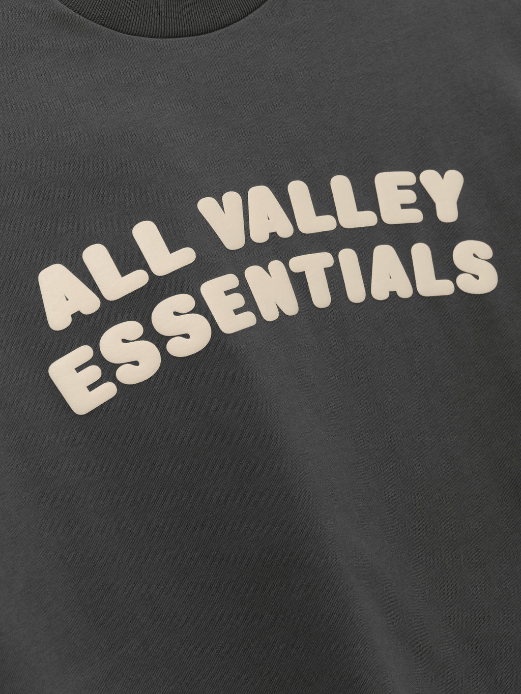 Kids Merch Tee in iron gray fabric featuring playful cream-colored bubble text "ALL VALLEY ESSENTIALS" across the front for a fun, casual kids' top.