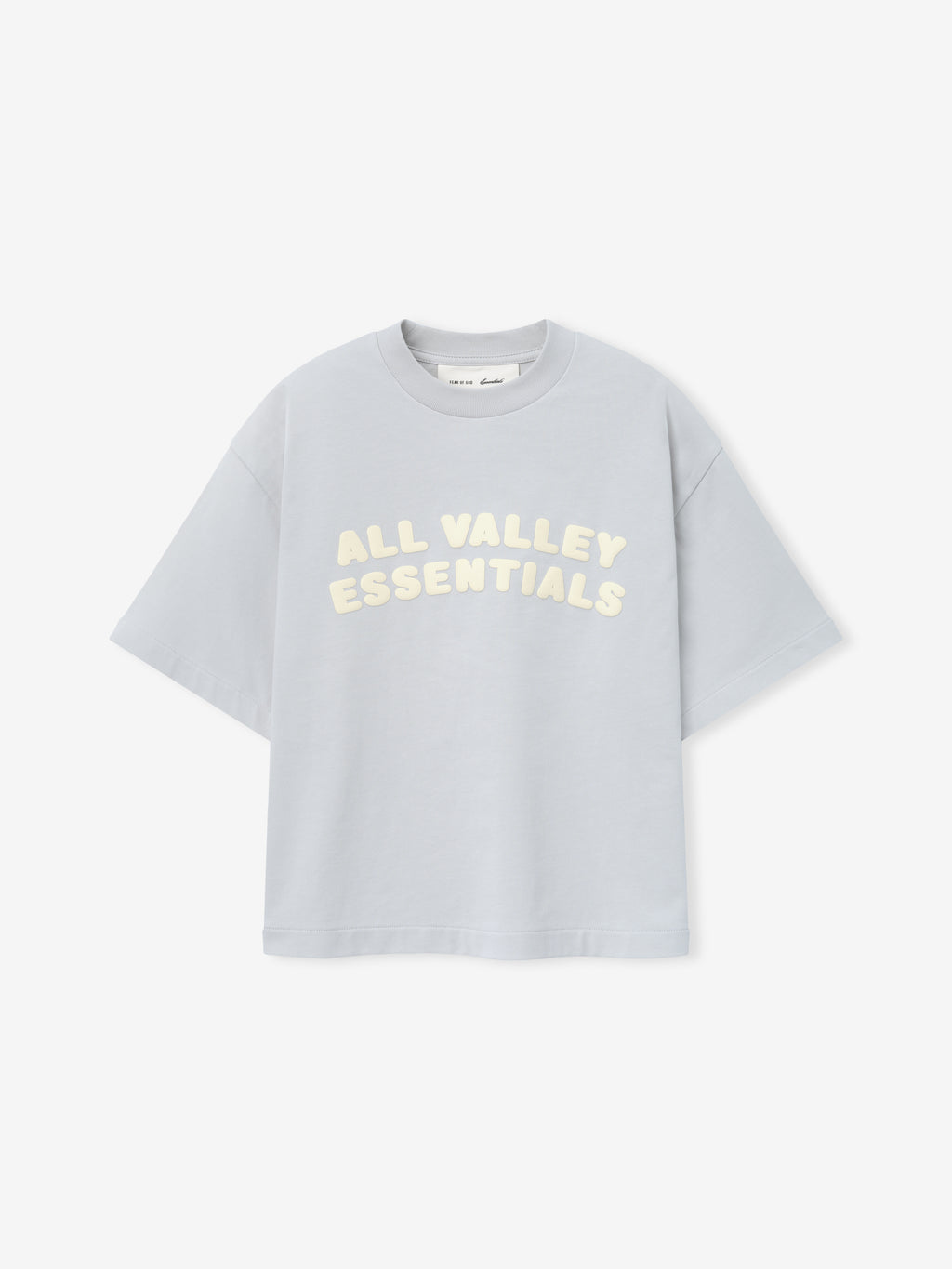 Kids Merch Tee in soft light gray fabric featuring cream-colored bubble lettering "ALL VALLEY ESSENTIALS" in a curved layout for a casual and playful kids' top.