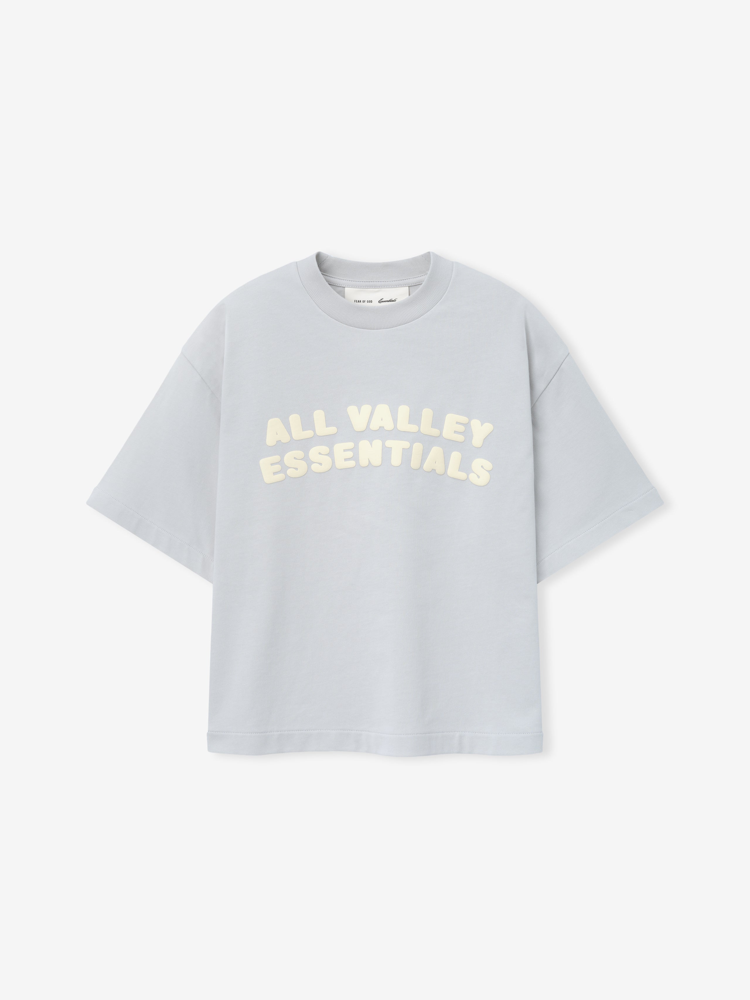 Kids Merch Tee in soft light gray fabric featuring cream-colored bubble lettering "ALL VALLEY ESSENTIALS" in a curved layout for a casual and playful kids' top.