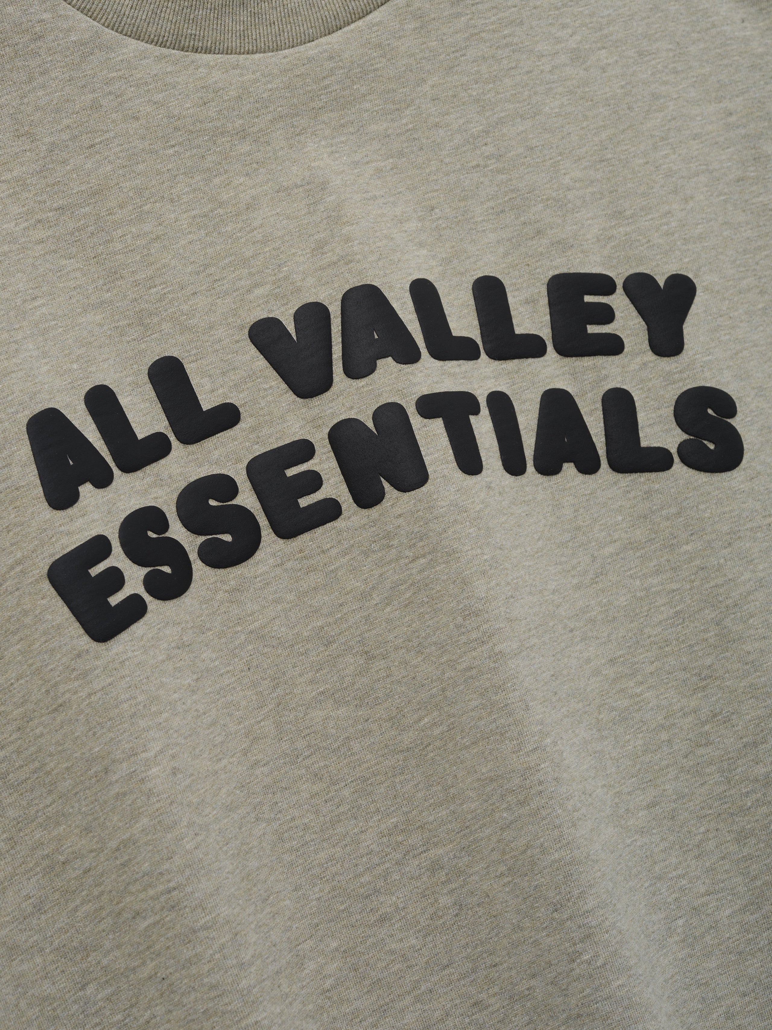 Kids Merch Tee in light heather gray fabric featuring bold black bubble letters spelling "ALL VALLEY ESSENTIALS" in an arched design for a cozy casual kids' top.