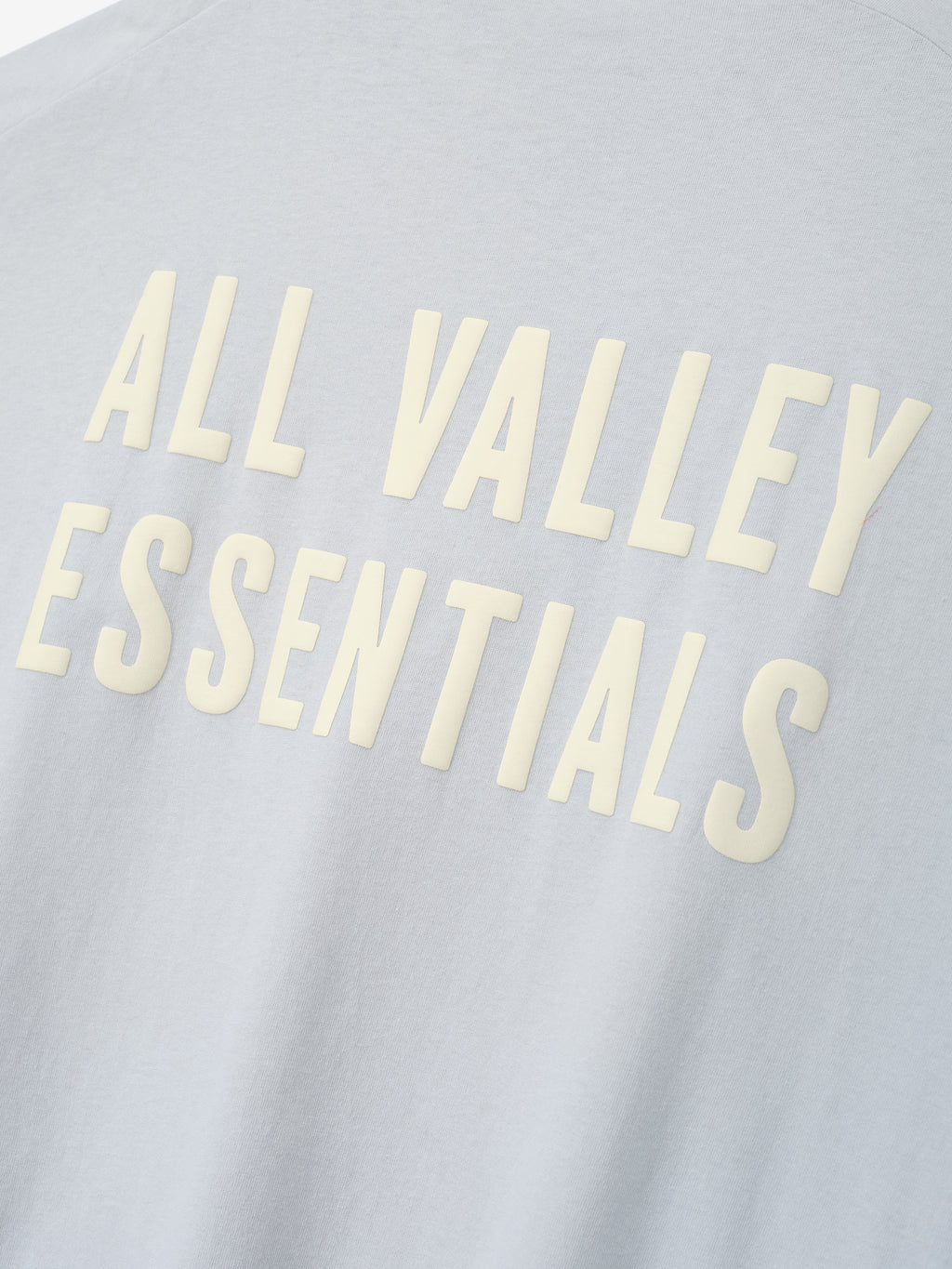 Close-up of Womens Long TShirt Dress fabric in soft light gray featuring raised cream-colored lettering reading "ALL VALLEY ESSENTIALS" in a clean, bold font.