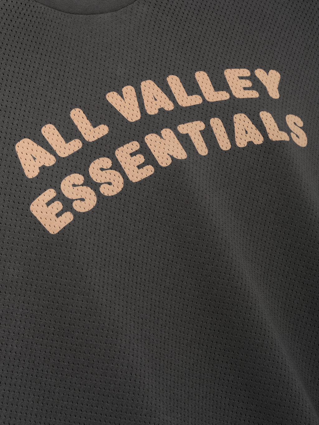 Womens Sport Mesh Merch Tee in dark iron grey featuring breathable mesh fabric with soft peach "ALL VALLEY ESSENTIALS" text in a rounded arch for a sporty casual top.