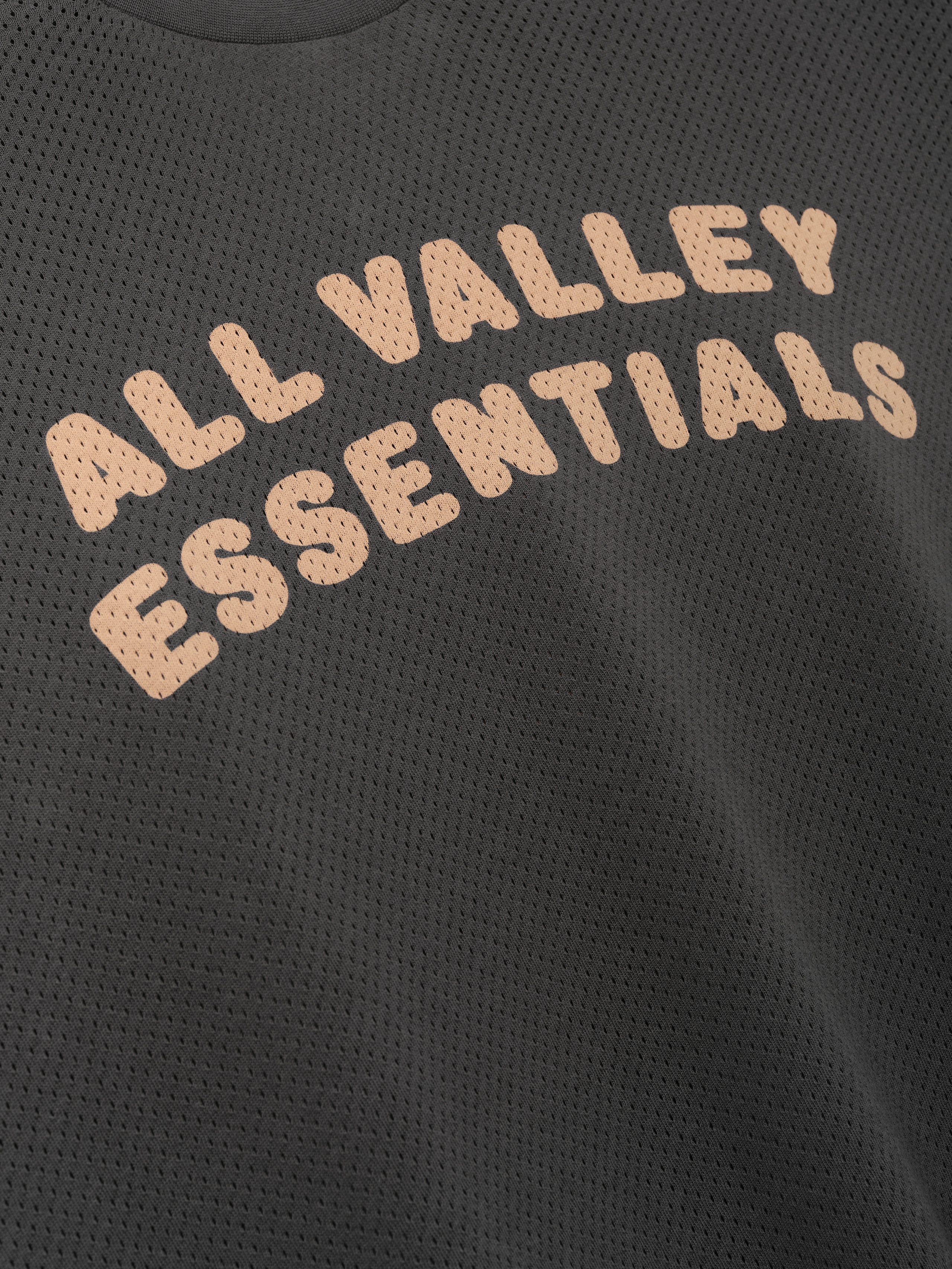 Womens Sport Mesh Merch Tee in dark iron grey featuring breathable mesh fabric with soft peach "ALL VALLEY ESSENTIALS" text in a rounded arch for a sporty casual top.