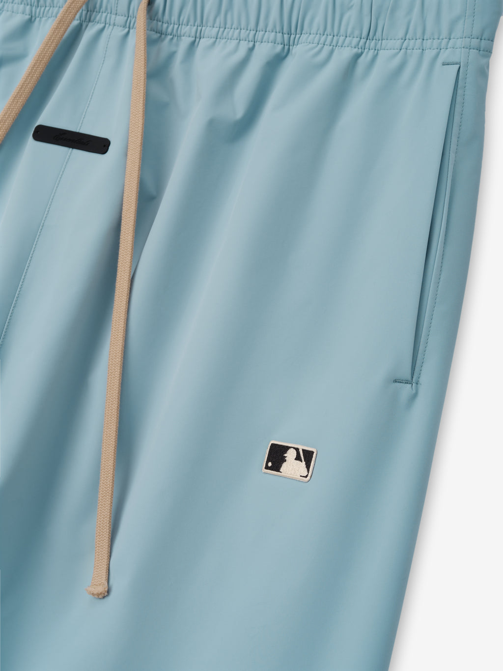 Mlb Relaxed Track Pant in light stone blue with beige drawstrings at the elastic waistband, side pockets, and a small contrasting MLB logo patch, crafted as casual bottoms.
