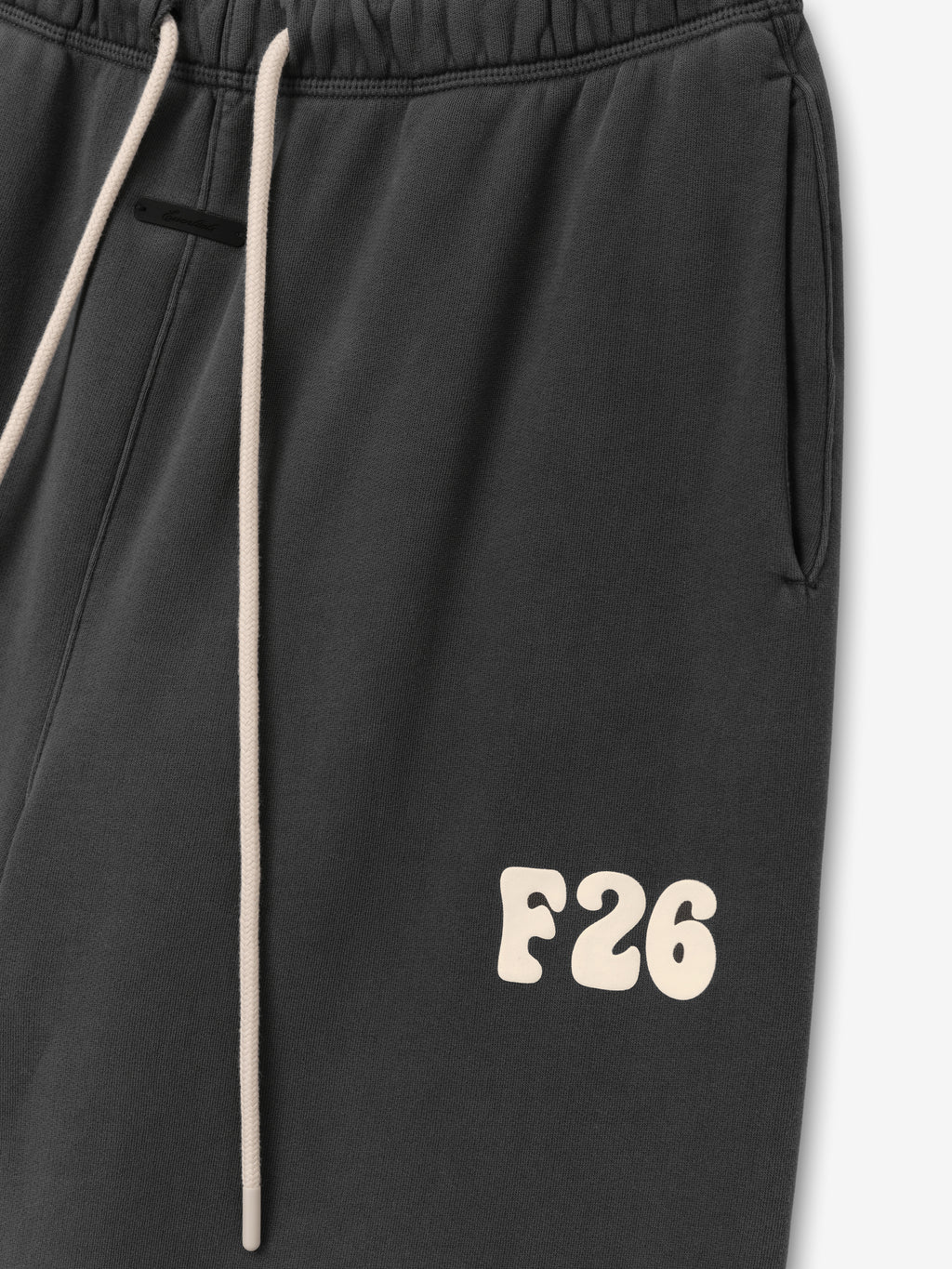 Close-up of Womens Classic Fleece Sweatpant in washed iron grey featuring an elastic waistband with drawstrings and a cream “F26” printed detail near the pocket for a sporty look.