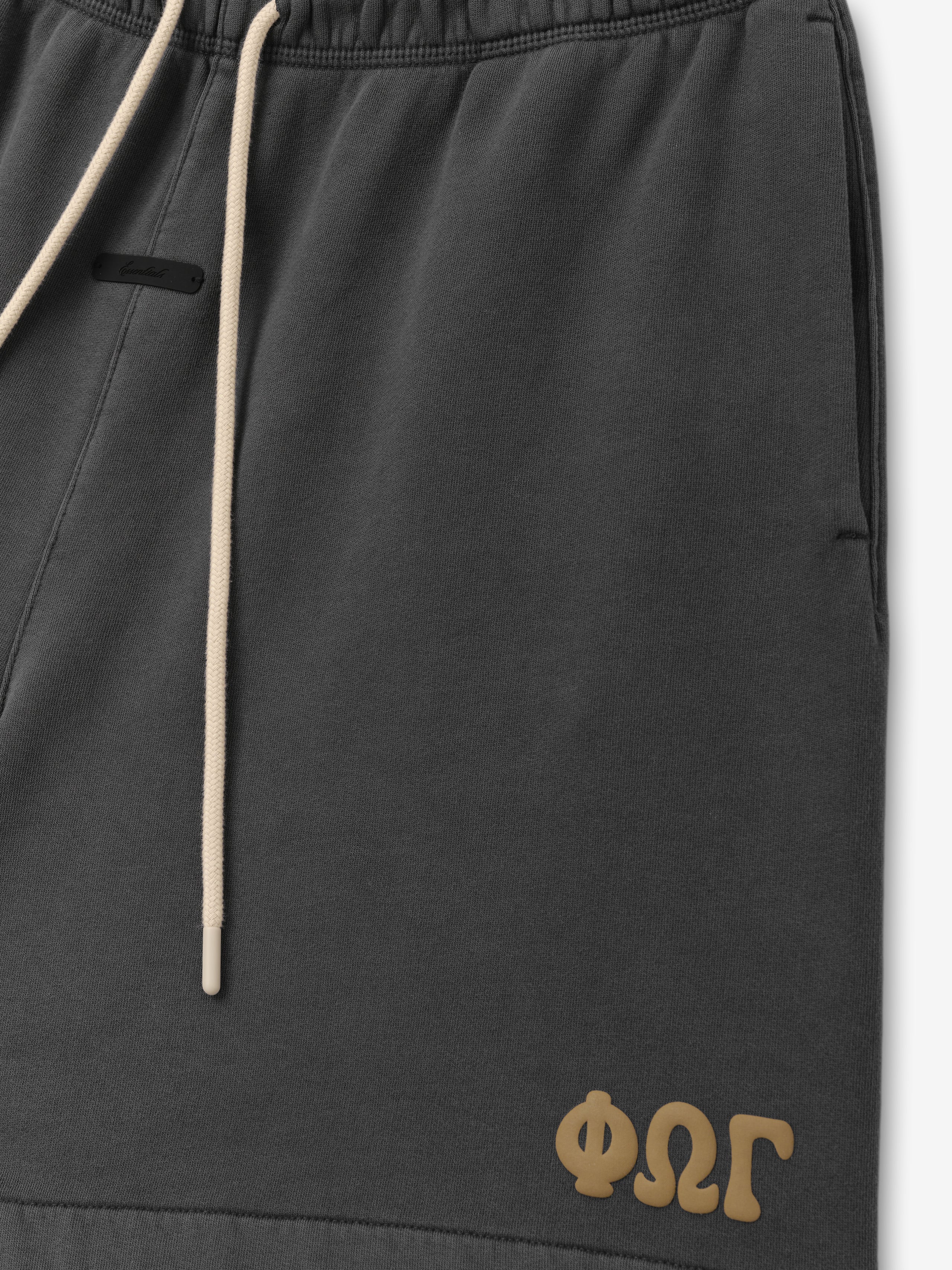Classic Sweatshort in a washed iron grey shade with an adjustable natural drawstring waistband, side pockets, and a distinctive gold Greek letter logo on the lower hem for casual bottoms.