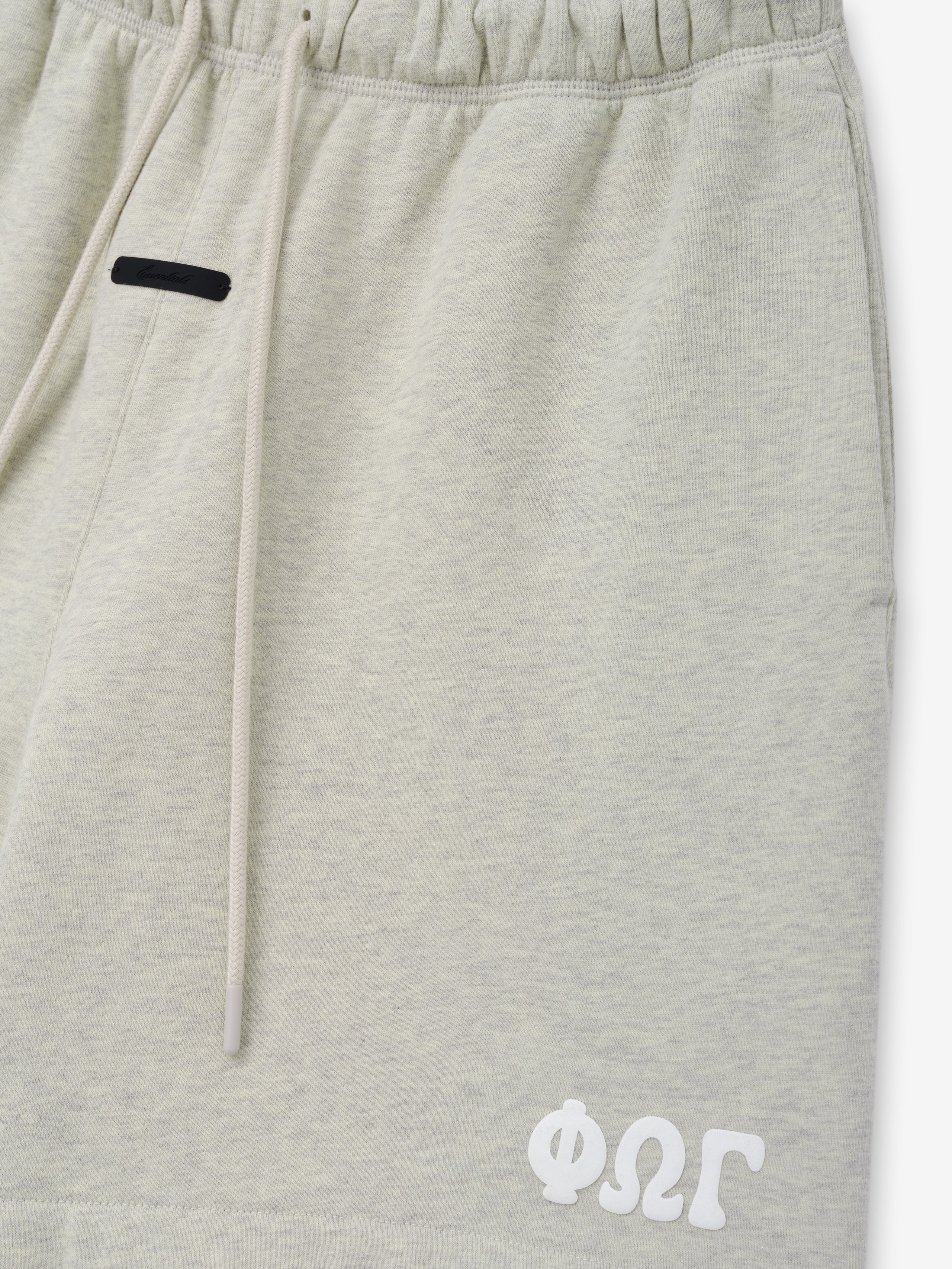 Classic Sweatshort in a soft light vanilla heather shade, featuring an elastic waistband with long drawstrings, side pockets, and a distinctive white stitched logo on the lower hem for casual bottoms.