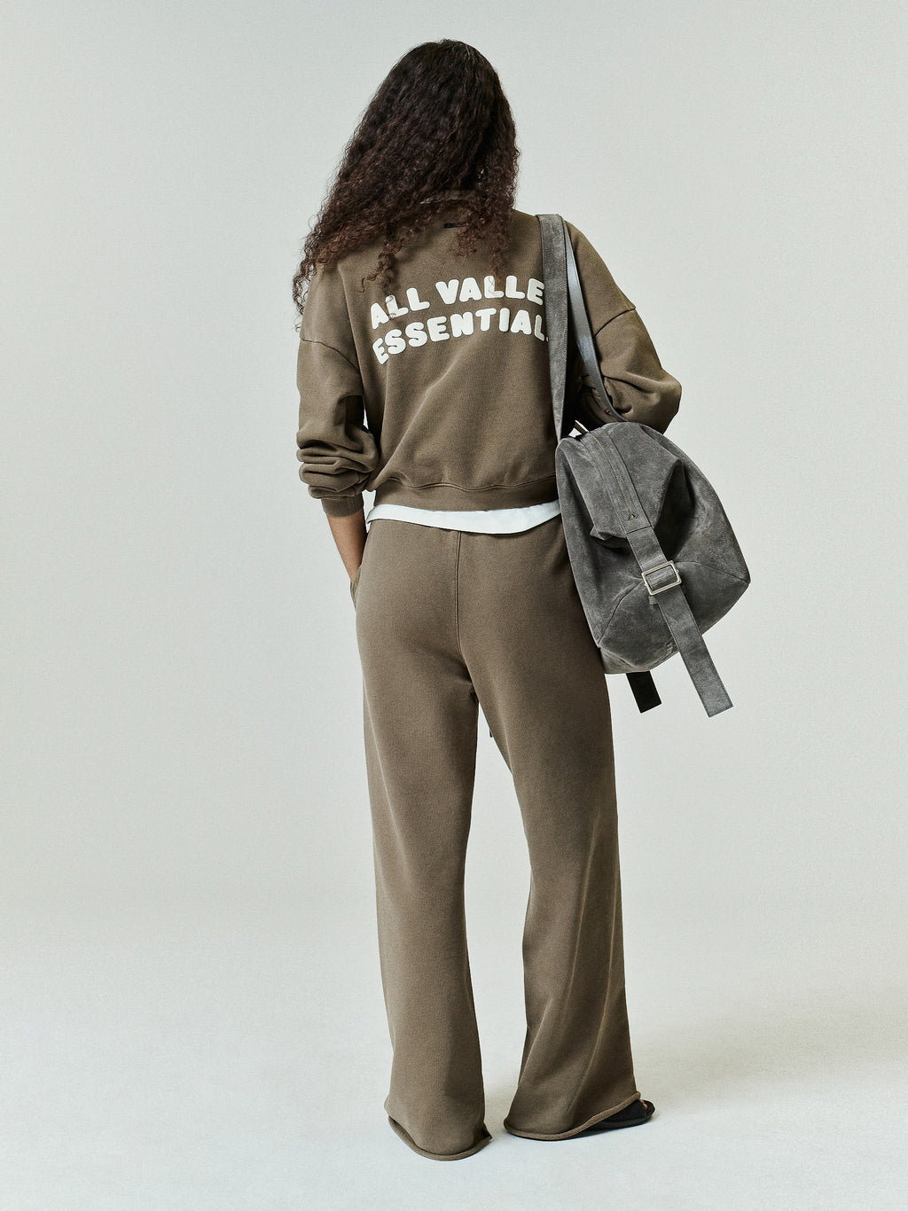 Womens French Terry Relaxed Half Zip in a muted olive tone, styled with relaxed fit pants and a casual backpack, showcasing a comfortable, minimalist streetwear look.