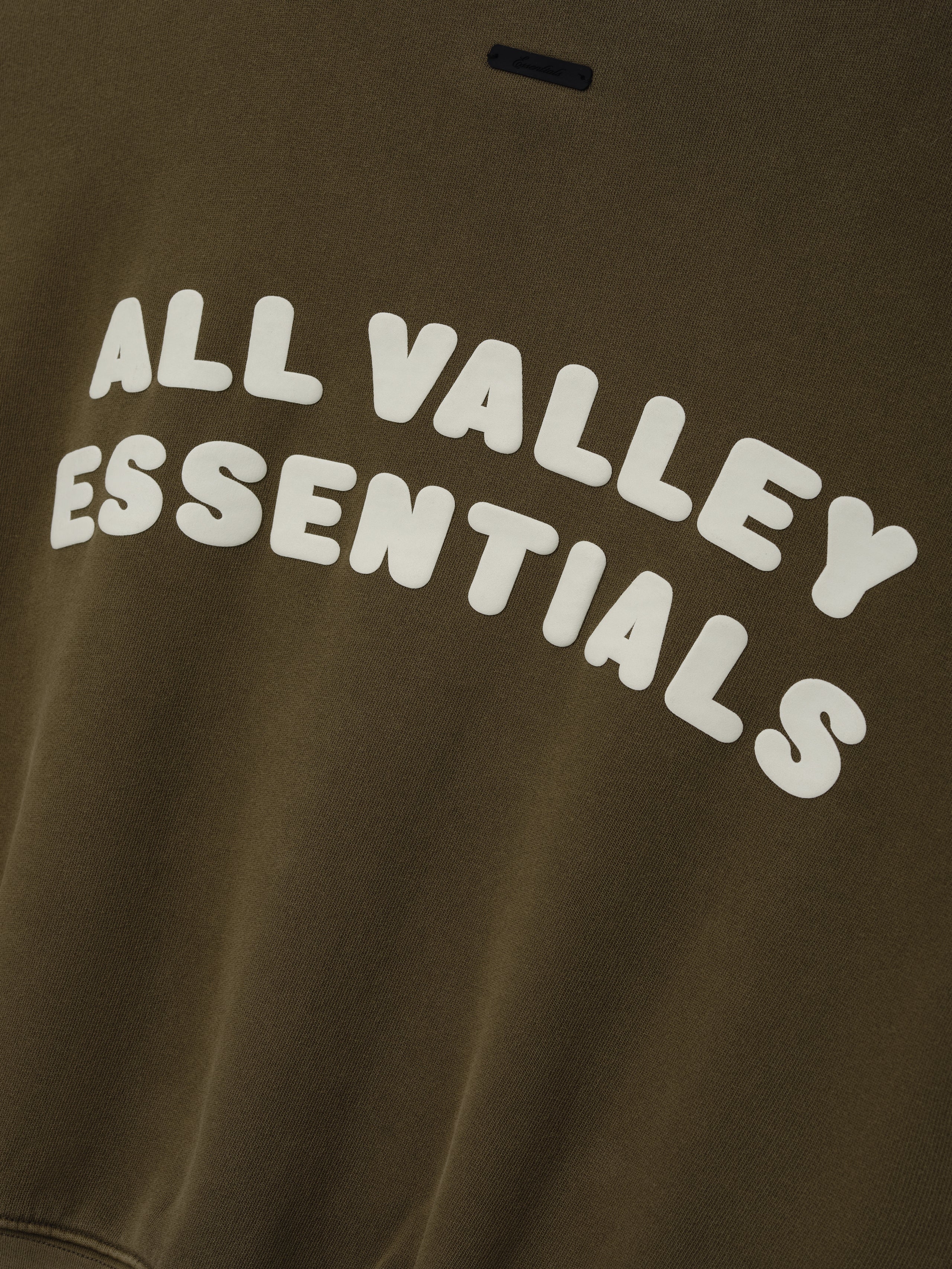 Womens French Terry Relaxed Half Zip in a muted olive green tone, featuring bold white embossed lettering “All Valley Essentials” across the chest for a stylish casual top.