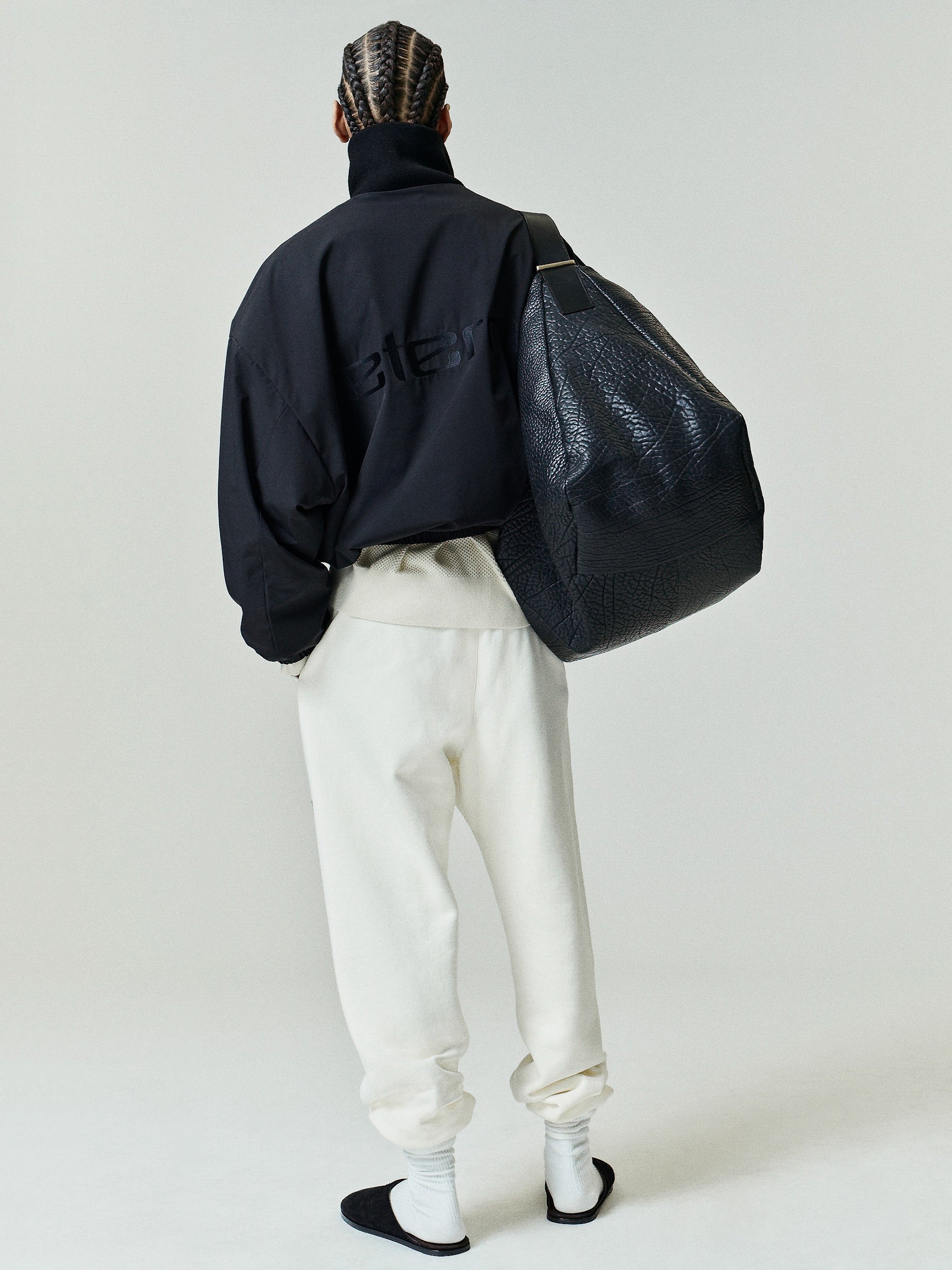 Classic Fleece Sweatpant in a soft washed ivory tone, featuring a relaxed fit with elastic cuffs and waistband, styled with black slides and a large textured black bag.