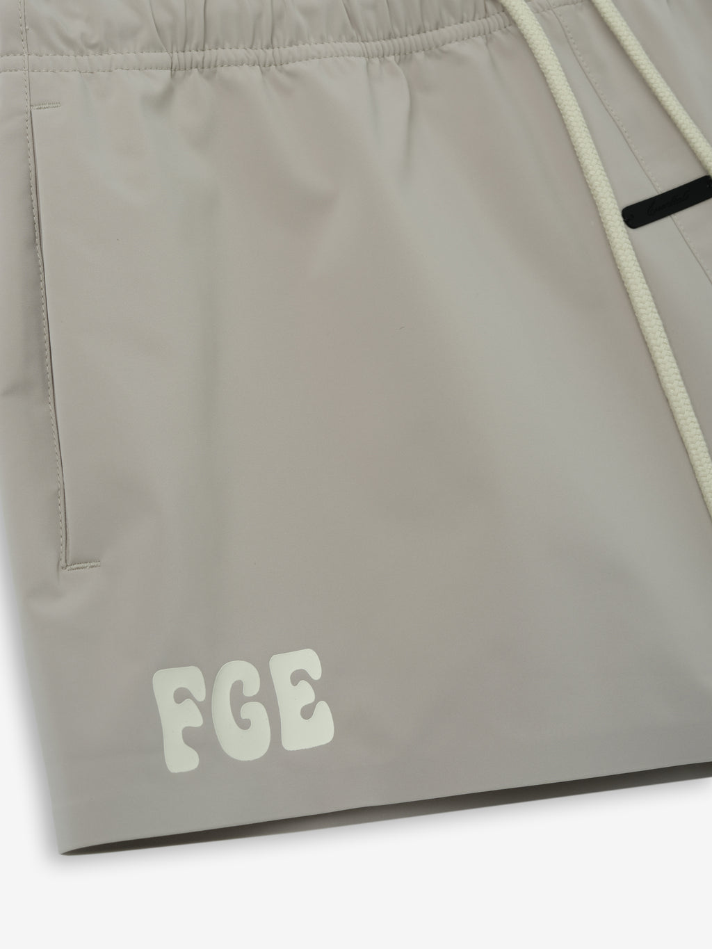Running Short in a soft muted beige shade, crafted from smooth fabric with an elastic waistband, functional side pockets, and subtle tonal branding for minimalist casual bottoms.