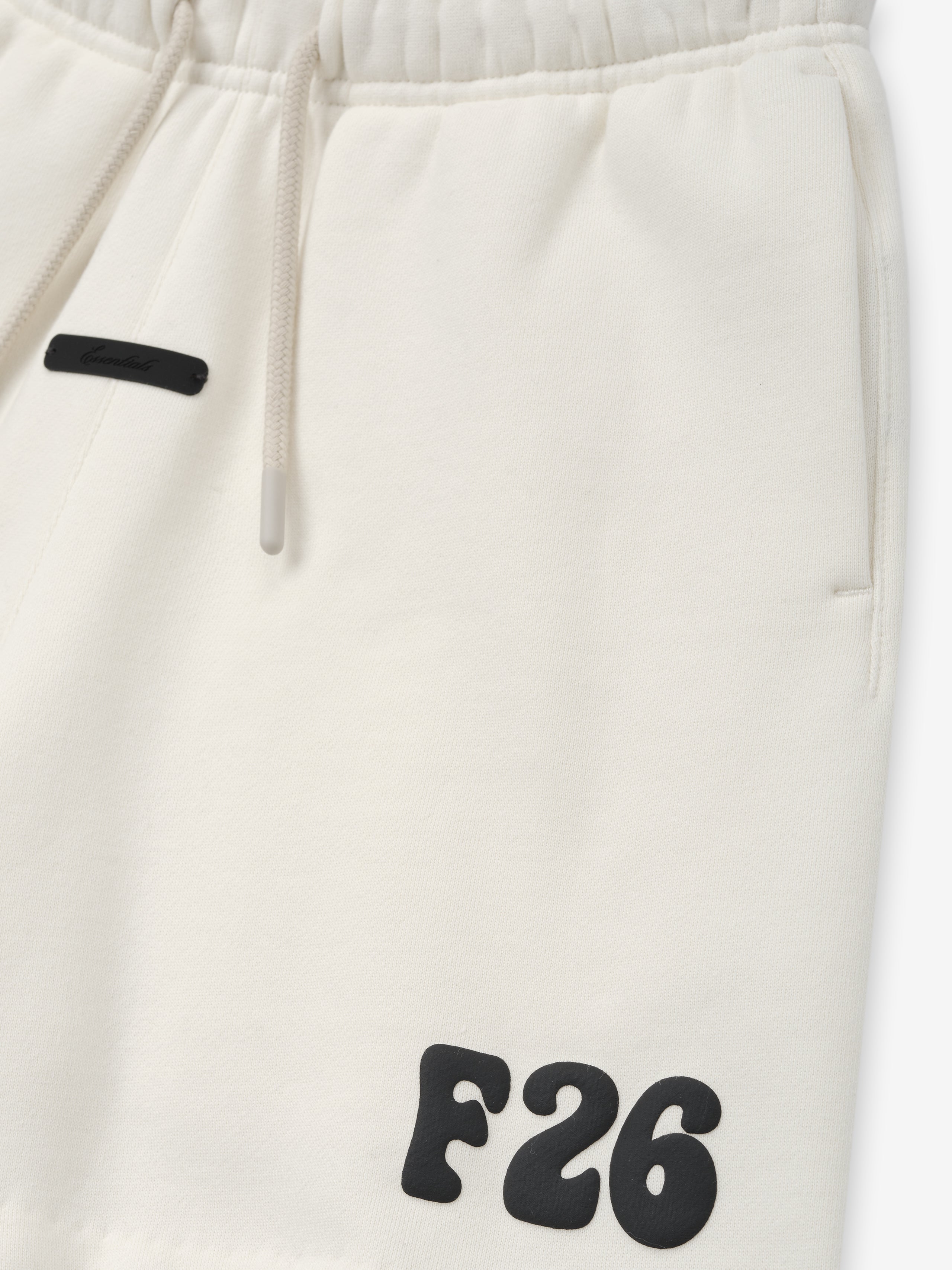 Kids Classic Sweatshort in a creamy ivory tone, featuring a soft elastic waistband with drawstrings, side pockets, and bold black "F26" printed detail for stylish kids bottoms.