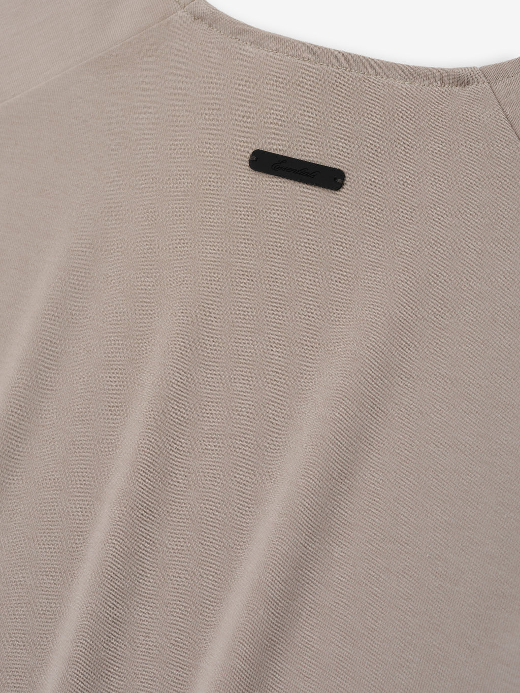 Soft Rib Fitted Tank in a soft muted beige tone, crafted from a smooth ribbed fabric with a minimalist back design and a small discreet logo plaque for subtle detail.