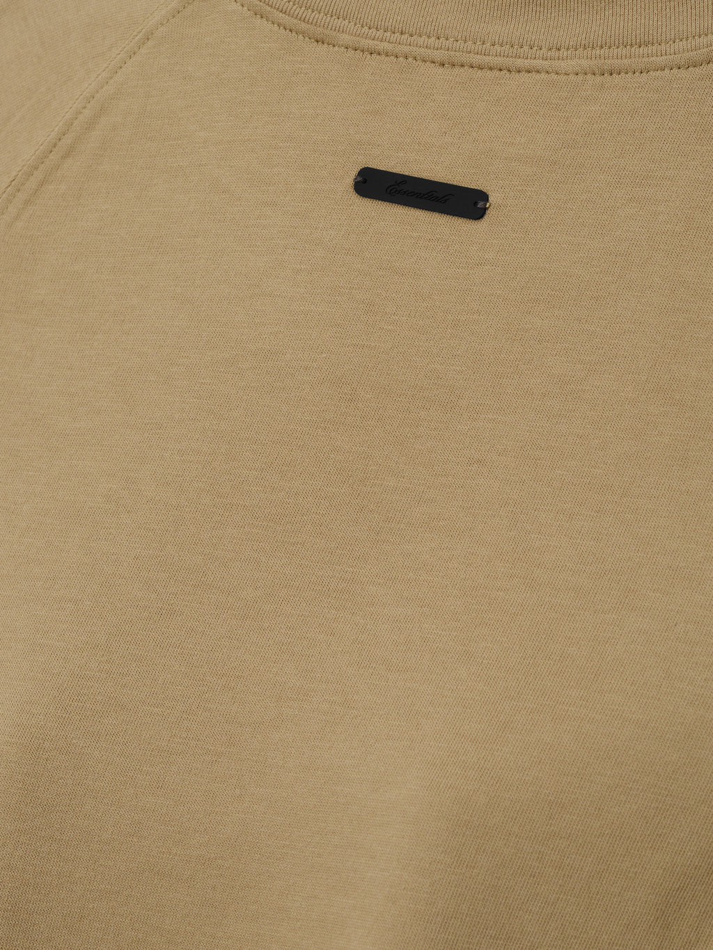Womens Tri-Blend Shrunken Baseball Tee in a muted dune tone with soft texture, featuring a small black branded patch near the neckline, crafted as a casual top.