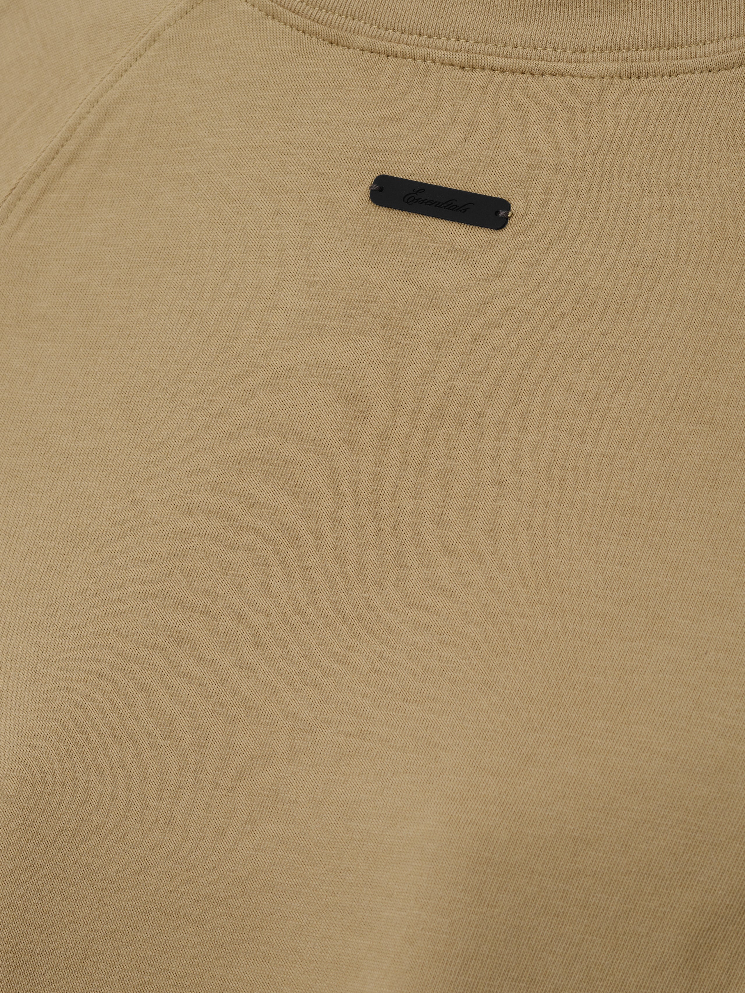 Womens Tri-Blend Shrunken Baseball Tee in a muted dune tone with soft texture, featuring a small black branded patch near the neckline, crafted as a casual top.