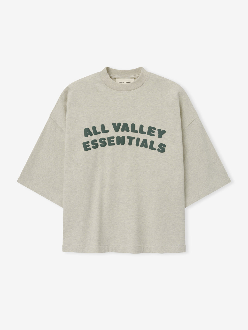 Merch Tee in soft vanilla heather featuring relaxed fit and oversized dark green "ALL VALLEY ESSENTIALS" lettering across the chest for a casual stylish top.