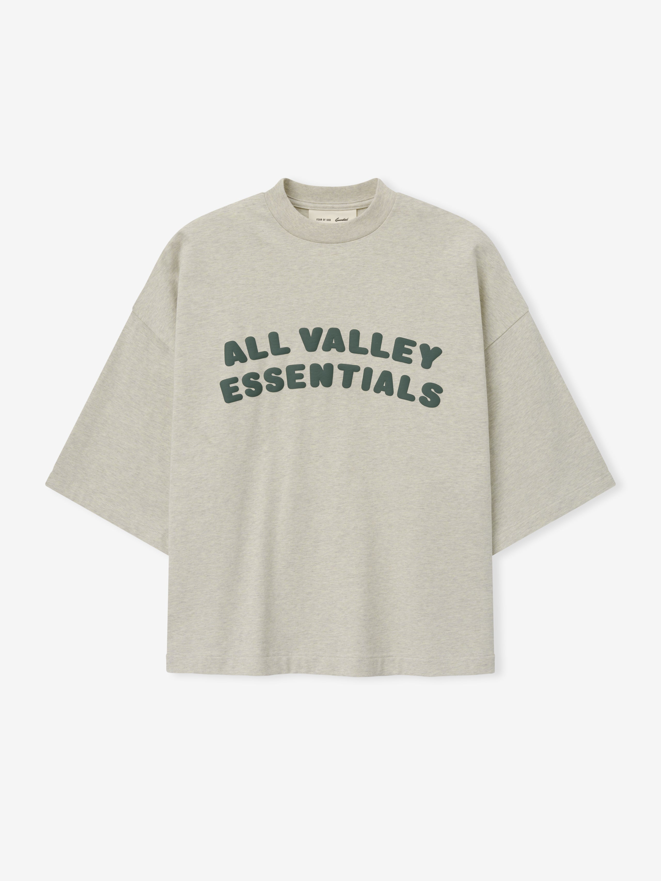 Merch Tee in soft vanilla heather featuring relaxed fit and oversized dark green "ALL VALLEY ESSENTIALS" lettering across the chest for a casual stylish top.