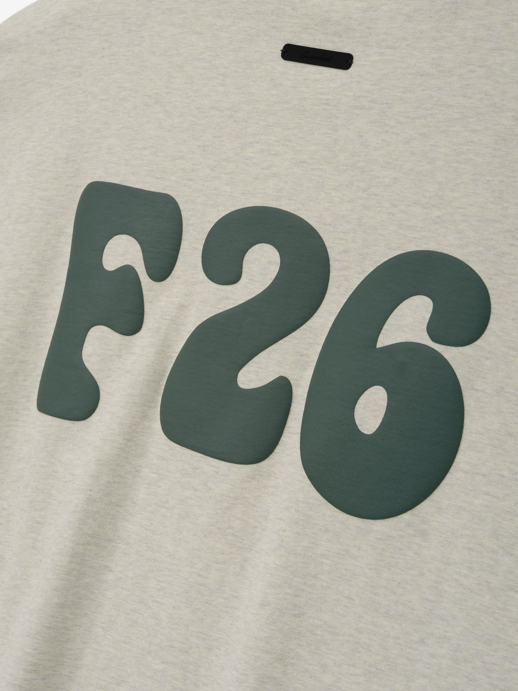Merch Tee in a soft vanilla heather color featuring bold dark green stylized "F26" lettering with a relaxed fit for a casual everyday top.