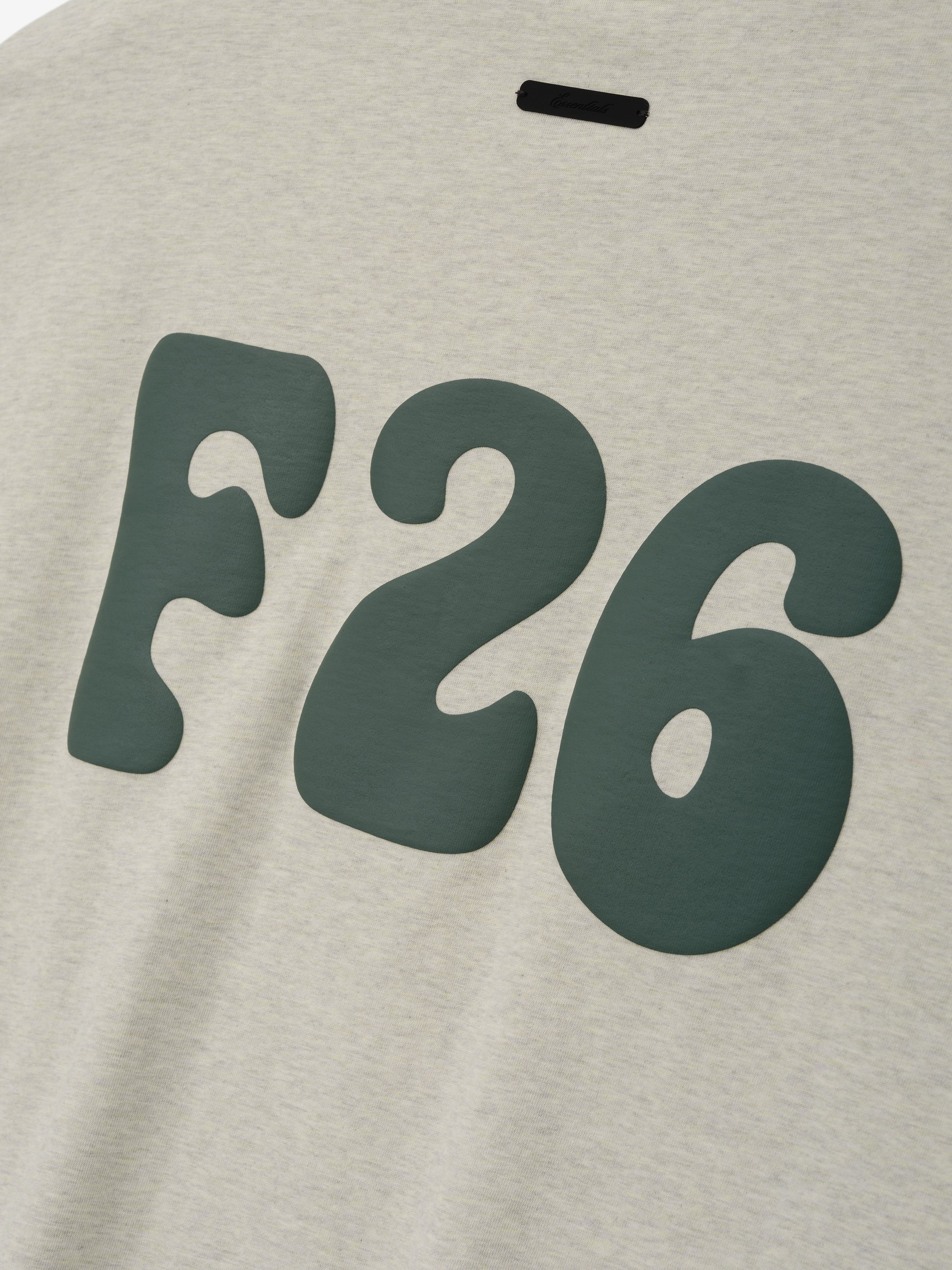 Merch Tee in a soft vanilla heather color featuring bold dark green stylized "F26" lettering with a relaxed fit for a casual everyday top.