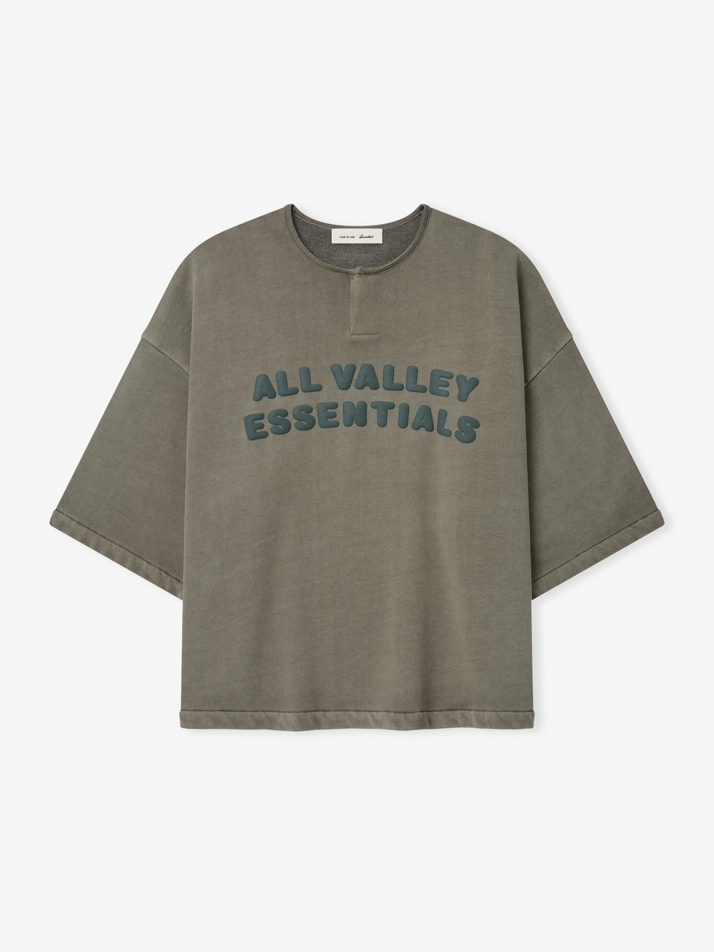 Front view of an olive washed 3/4 Henley Sweatshirt with dropped shoulders, wide sleeves, and raised teal lettering reading "ALL VALLEY ESSENTIALS" across the chest.
