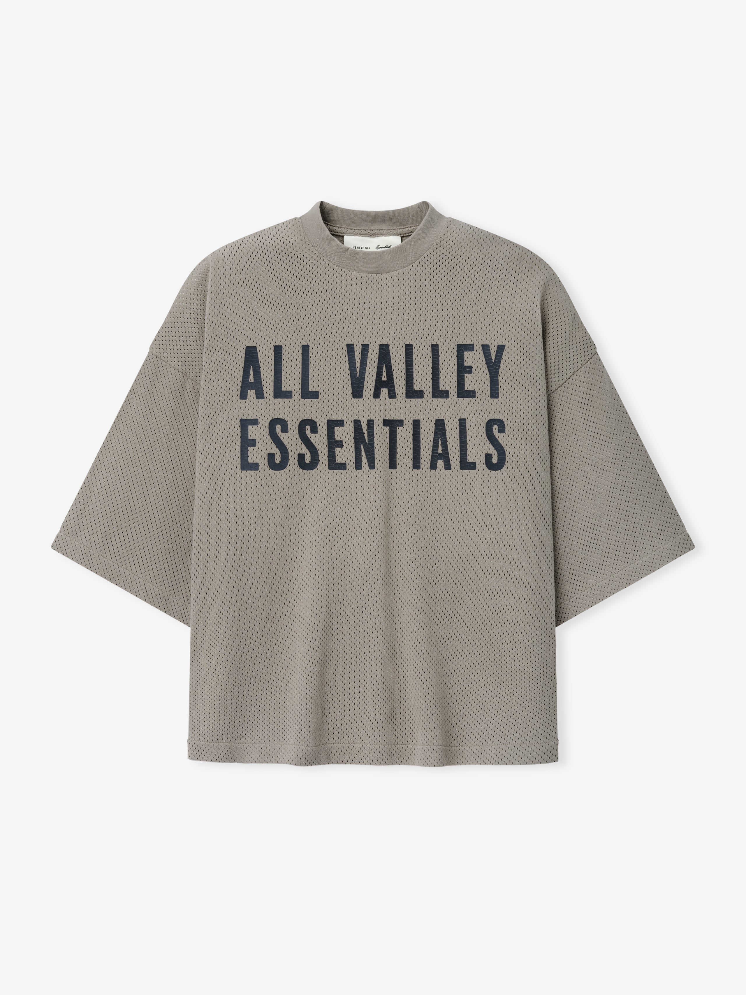 Merch Tee in muted taupe with a textured knit fabric and bold black "ALL VALLEY ESSENTIALS" text printed on the front for a modern and relaxed casual top.