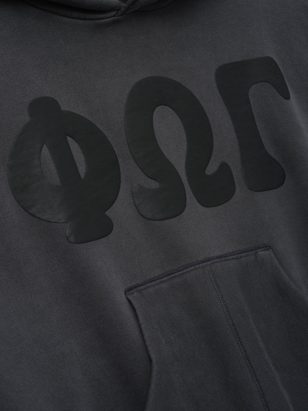Womens 90s Fleece Hoodie in dark washed iron grey featuring a close-up of the front with subtle tonal Greek letters and a softly textured kangaroo pocket.