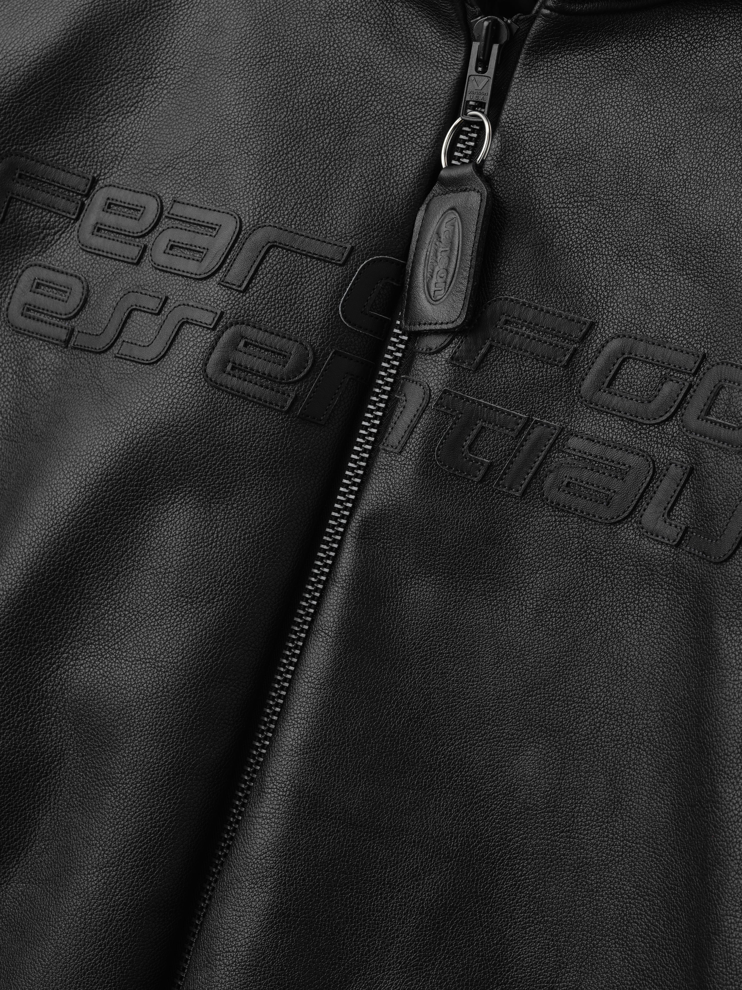 Close-up of a black leather jacket with 'Ferrari' branding on the zipper.