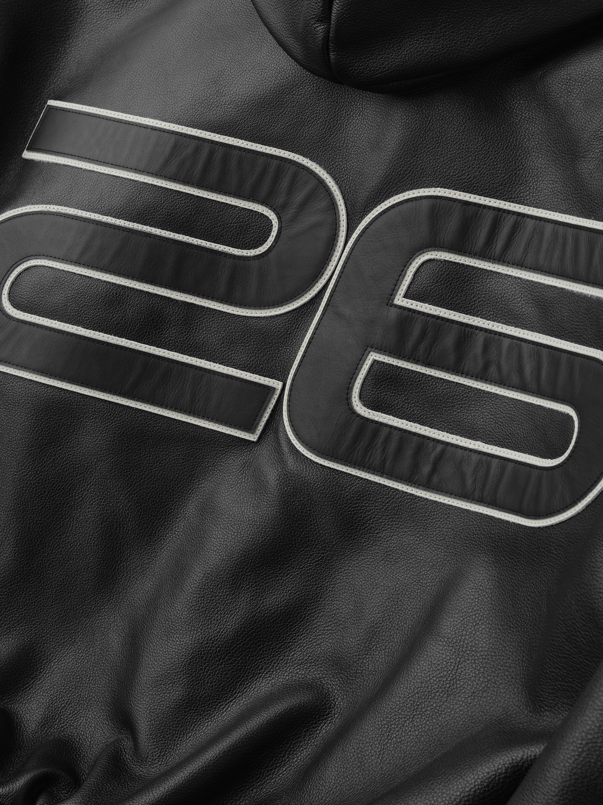 Black leather jacket with white stitching on a dark background