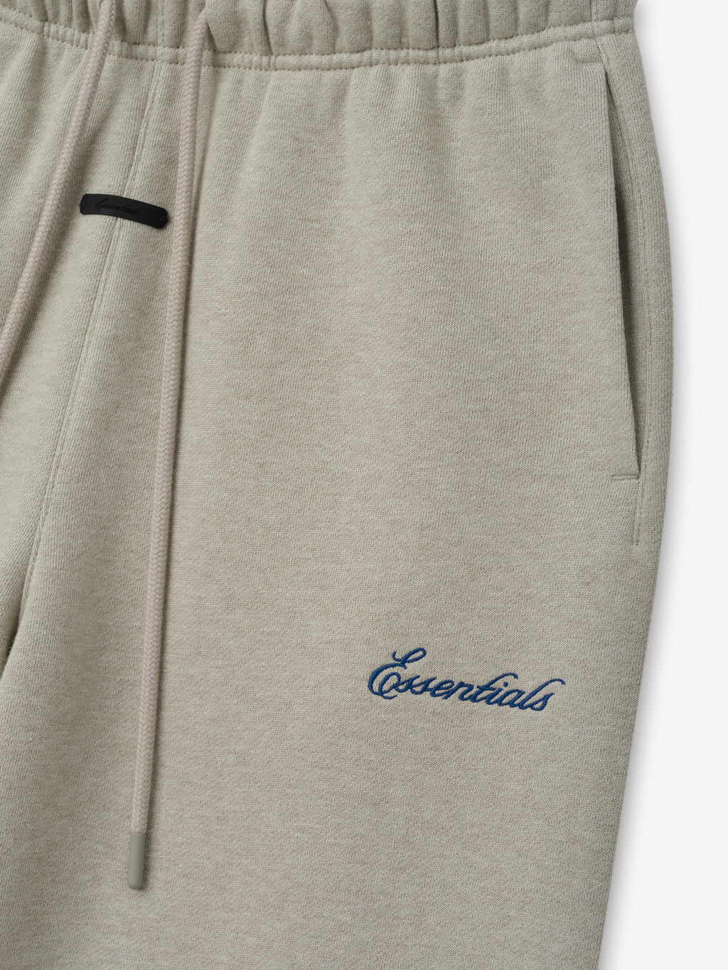 Womens Slim Sweatpant in stone shown close up with an elastic waistband drawstring side pocket and blue Essentials script branding as Bottoms