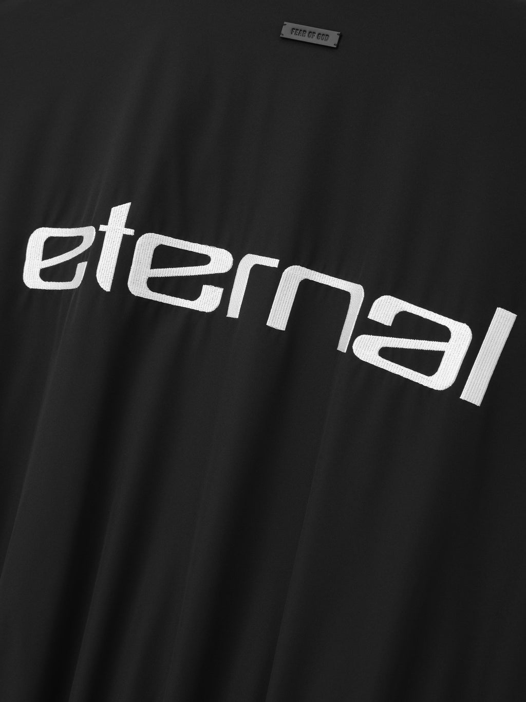 Bonded Nylon Tech Windbreaker in black shown in close detail with a large white Eternal graphic and Fear of God label on smooth nylon fabric as Outerwear