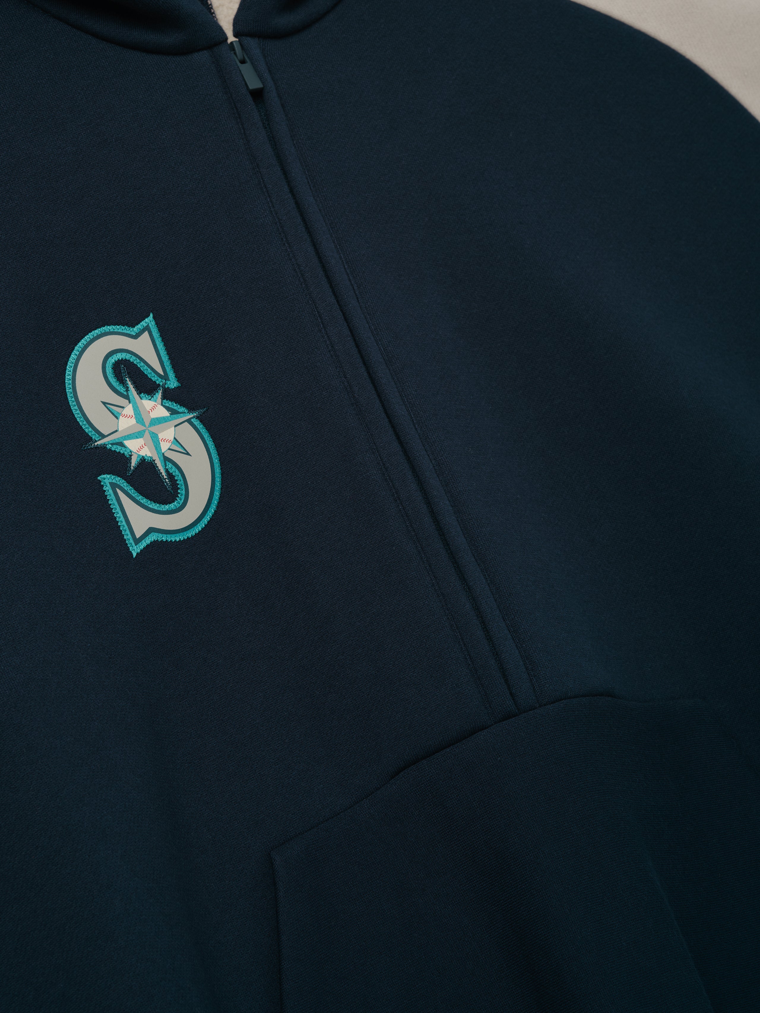 Close-up view of the Mariners Raglan Half Zip Sport Hoodie in dark sapphire, featuring a front half-zip design and a stitched stylized compass logo on the chest.