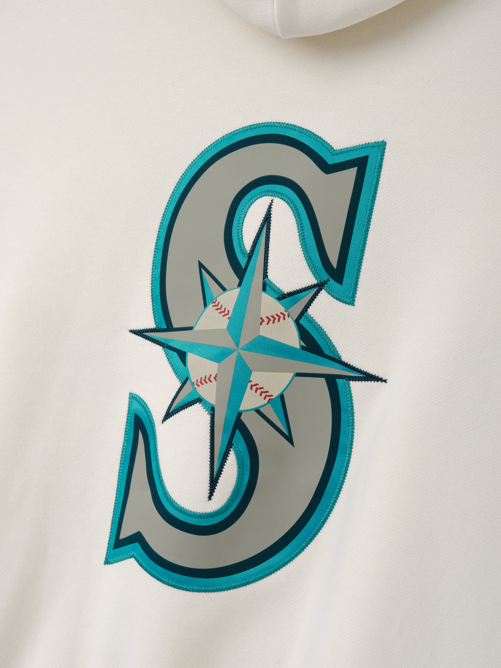 Close-up of the Mariners Sport Hoodie in soft white fabric, showcasing a large stitched "S" graphic with a teal and gray compass design featuring a baseball detail at the center.