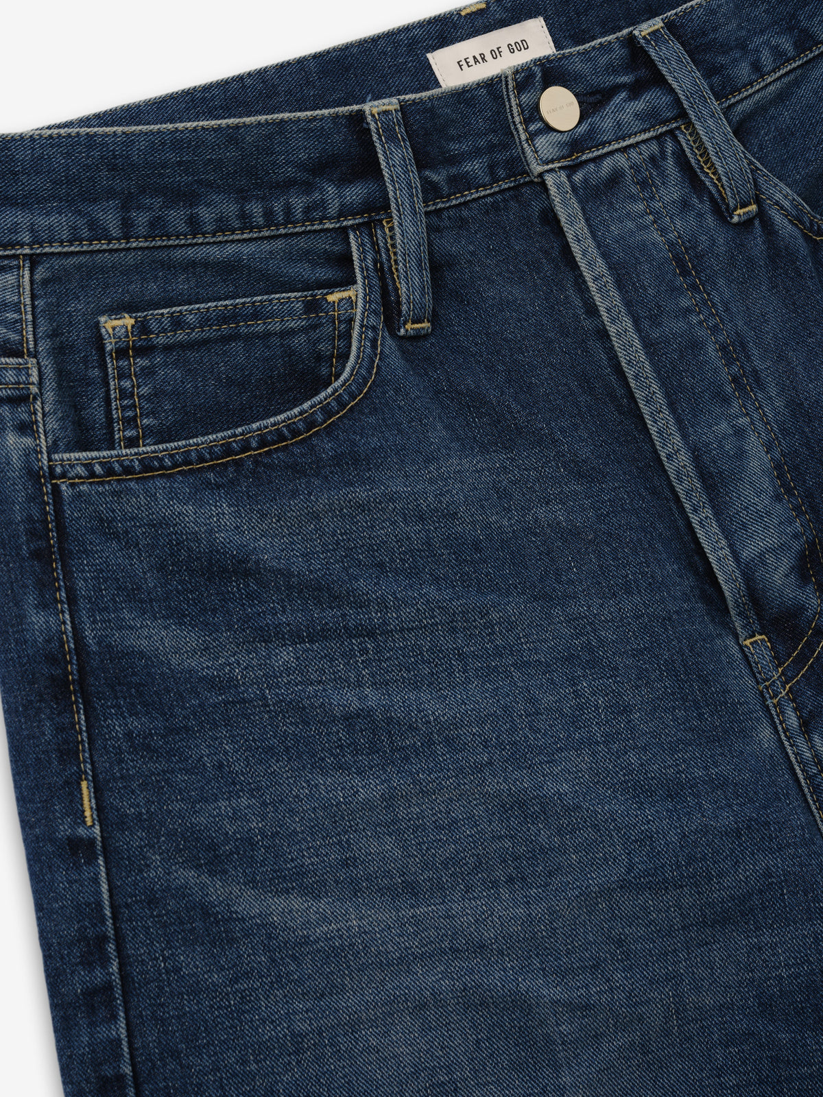 Relaxed Fit Jeans in dark blue denim shown in close detail with a Fear of God waistband label, belt loops, front pocket and button closure as Bottoms
