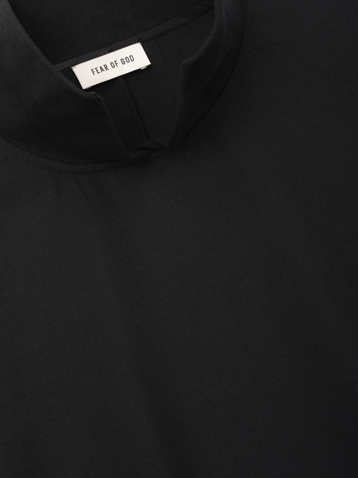 Wool Ripstop Pullover Shirt close up in black showing the neckline inner construction Fear of God label and subtle ripstop texture as Tops