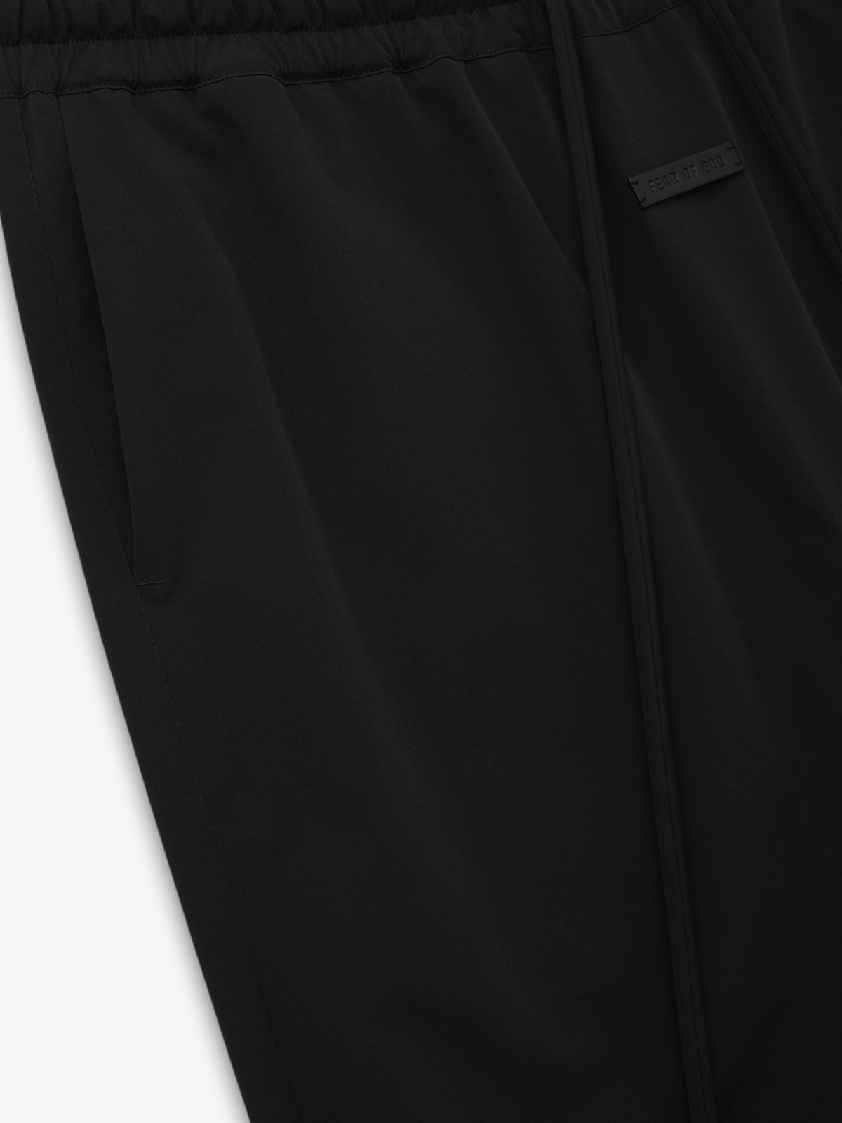 Bonded Nylon Track Pant close up in black showing the elastic waistband zip front closure side pocket and Fear of God label as Bottoms