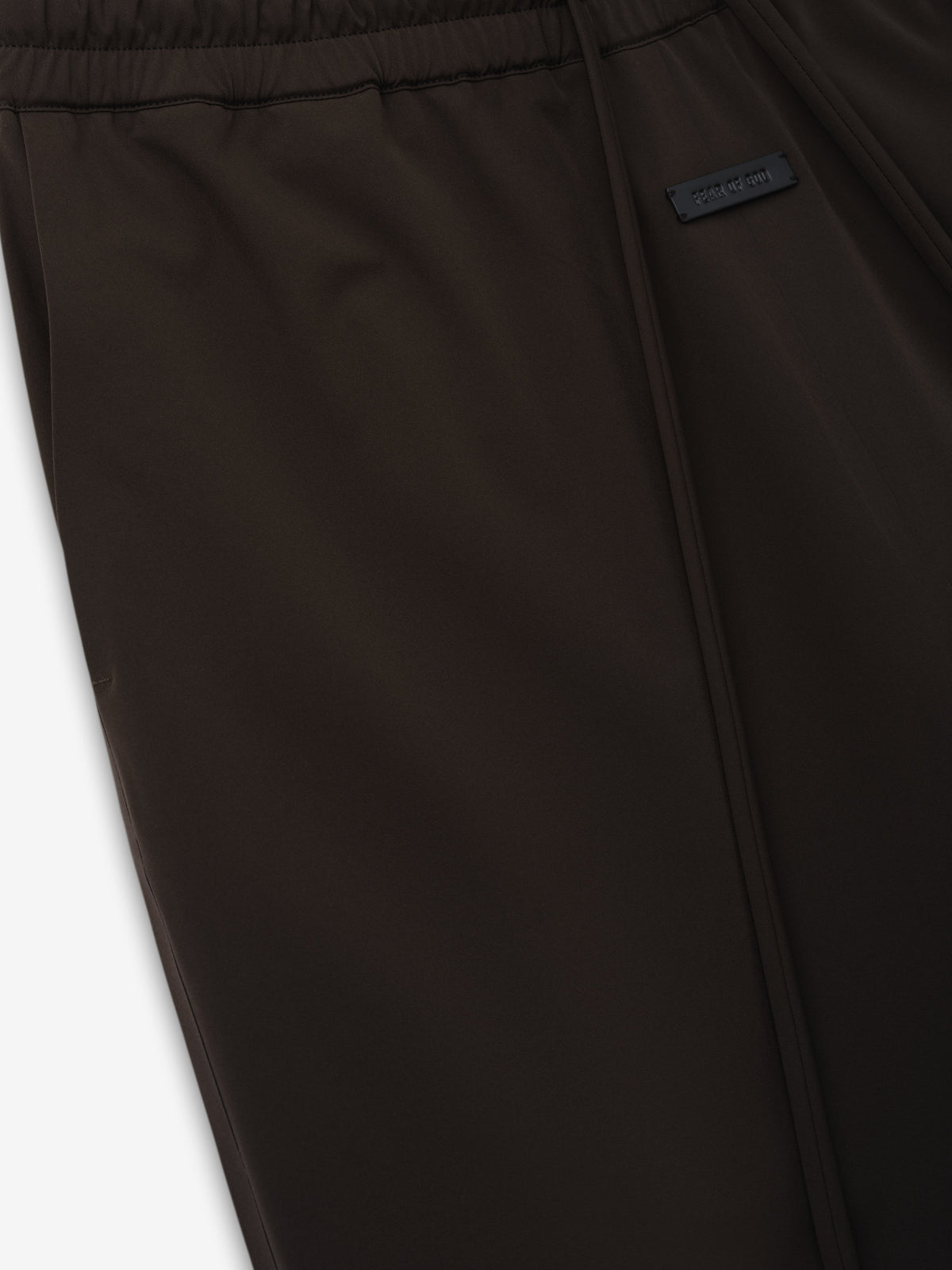 Bonded Nylon Track Pant close up in dark brown showing the elastic waistband zip pocket and Fear of God label as Bottoms