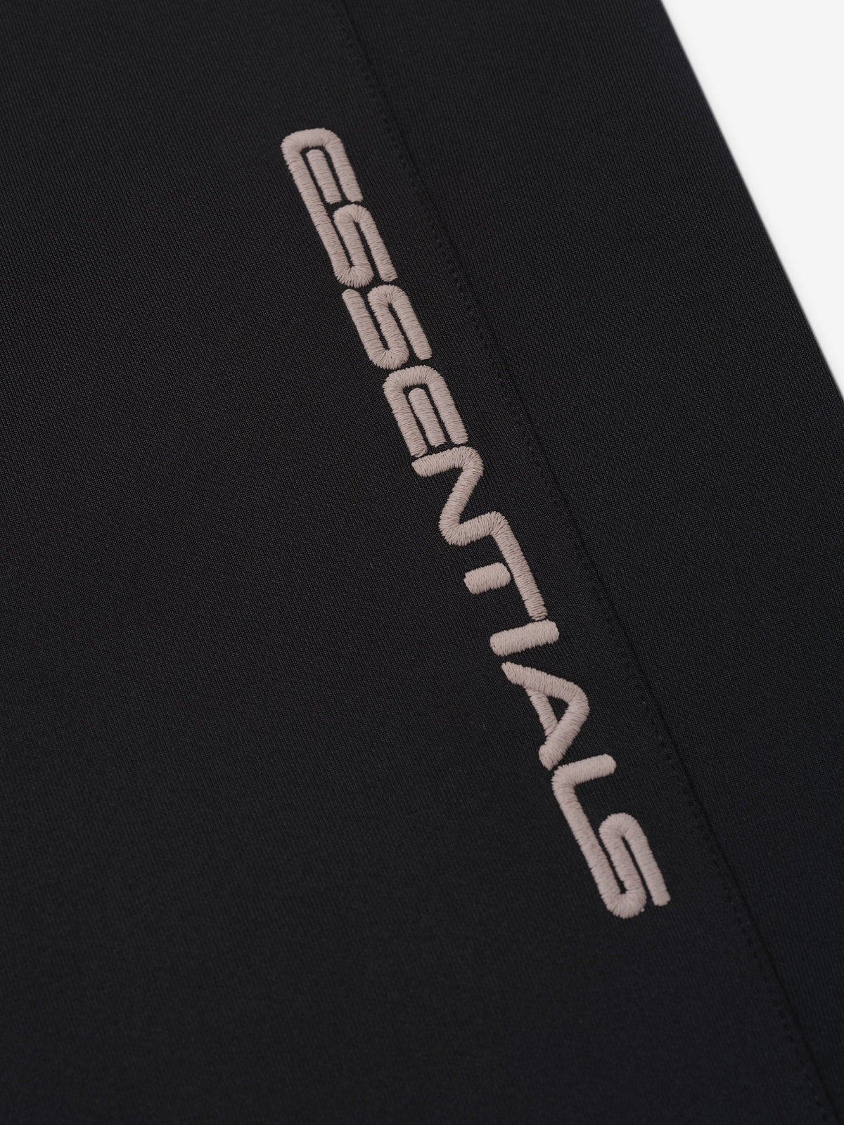 Womens Slim Trackpant close up in black featuring tonal Essentials branding along a seam with smooth structured fabric as Bottoms