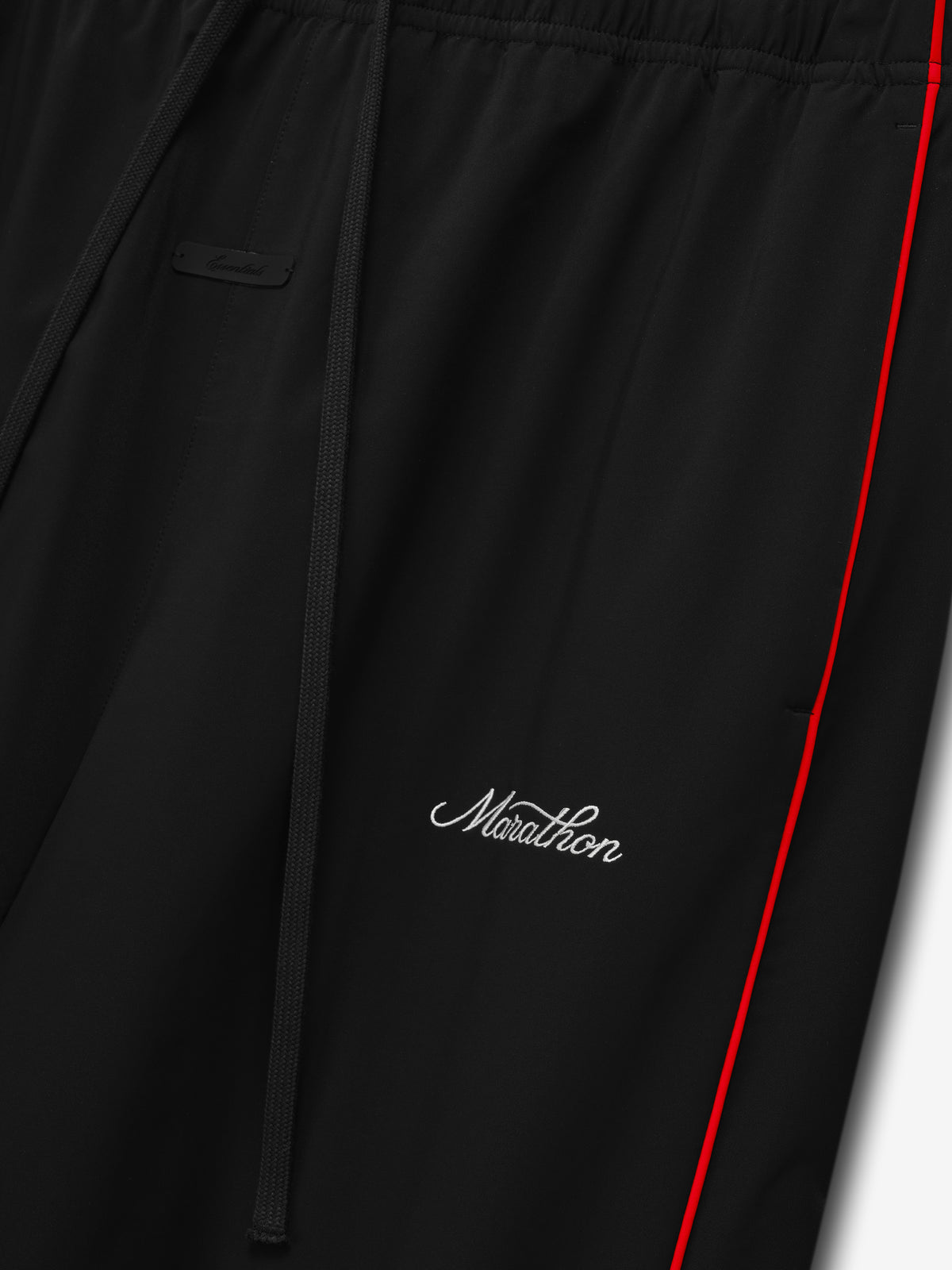 Marathon Relaxed Track Pant in black with red side piping drawstring waist and white Marathon script logo shown in close up as Bottoms