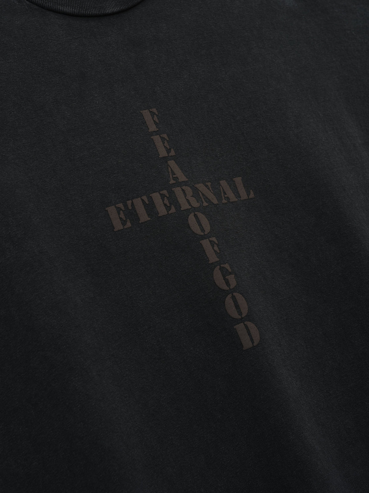 Cross Tee shown in close detail in black with tonal ETERNAL OF GOD text arranged in a cross shape on the chest as Tops