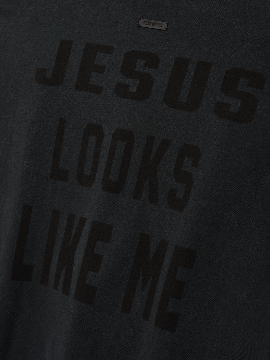 Cross Tee shown in close detail in black with a tonal JESUS LOOKS LIKE ME chest graphic and visible neck label as Tops