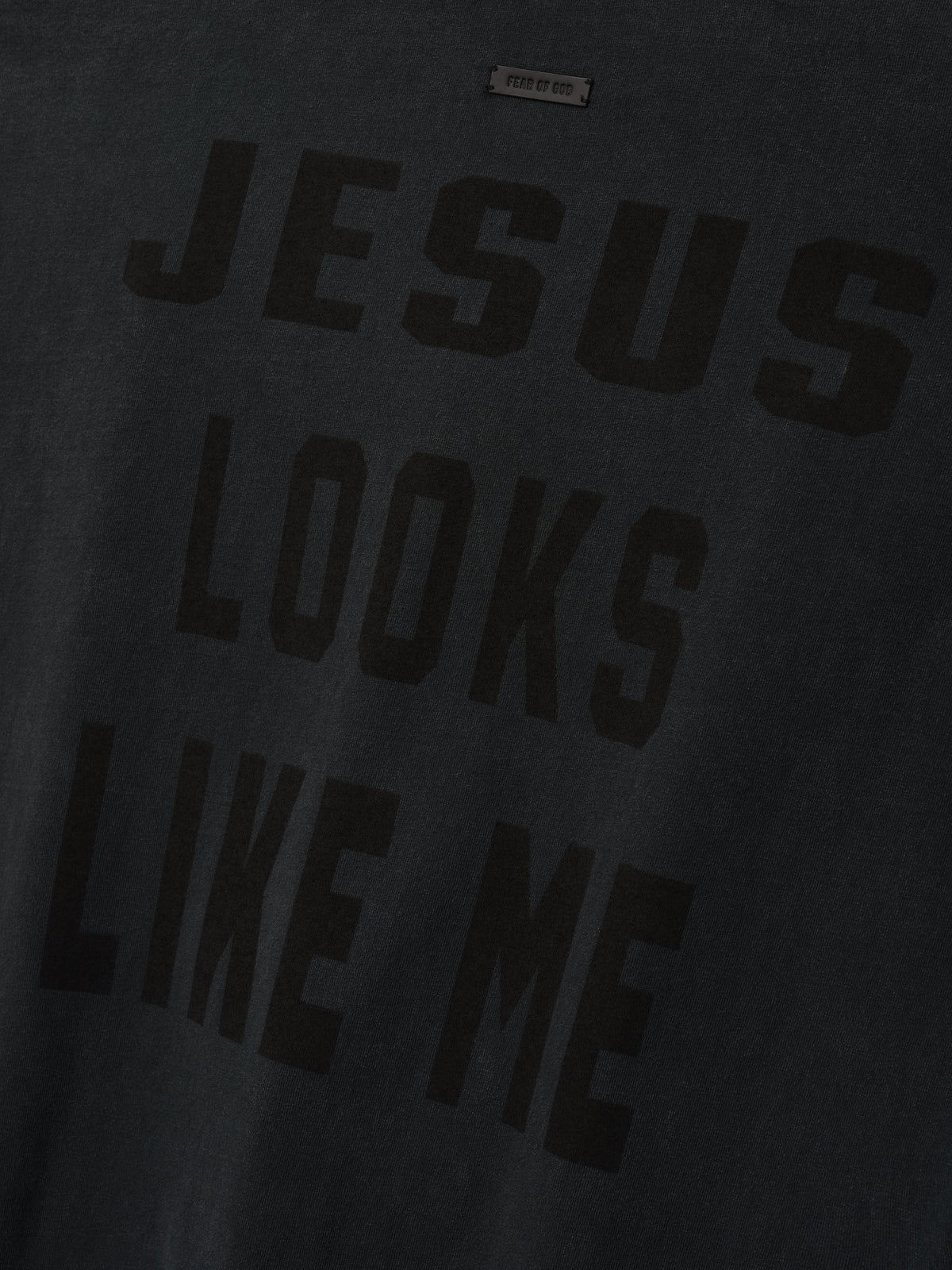 Cross Tee shown in close detail in black with a tonal JESUS LOOKS LIKE ME chest graphic and visible neck label as Tops