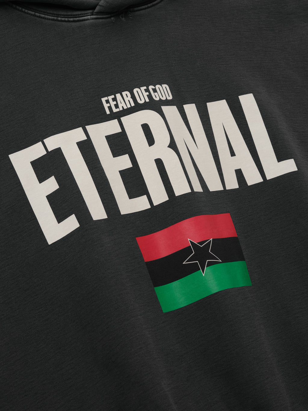 Reflection Eternal Hoodie in black featuring bold cream Eternal lettering Fear of God branding and a red green black flag graphic shown in close detail as Tops