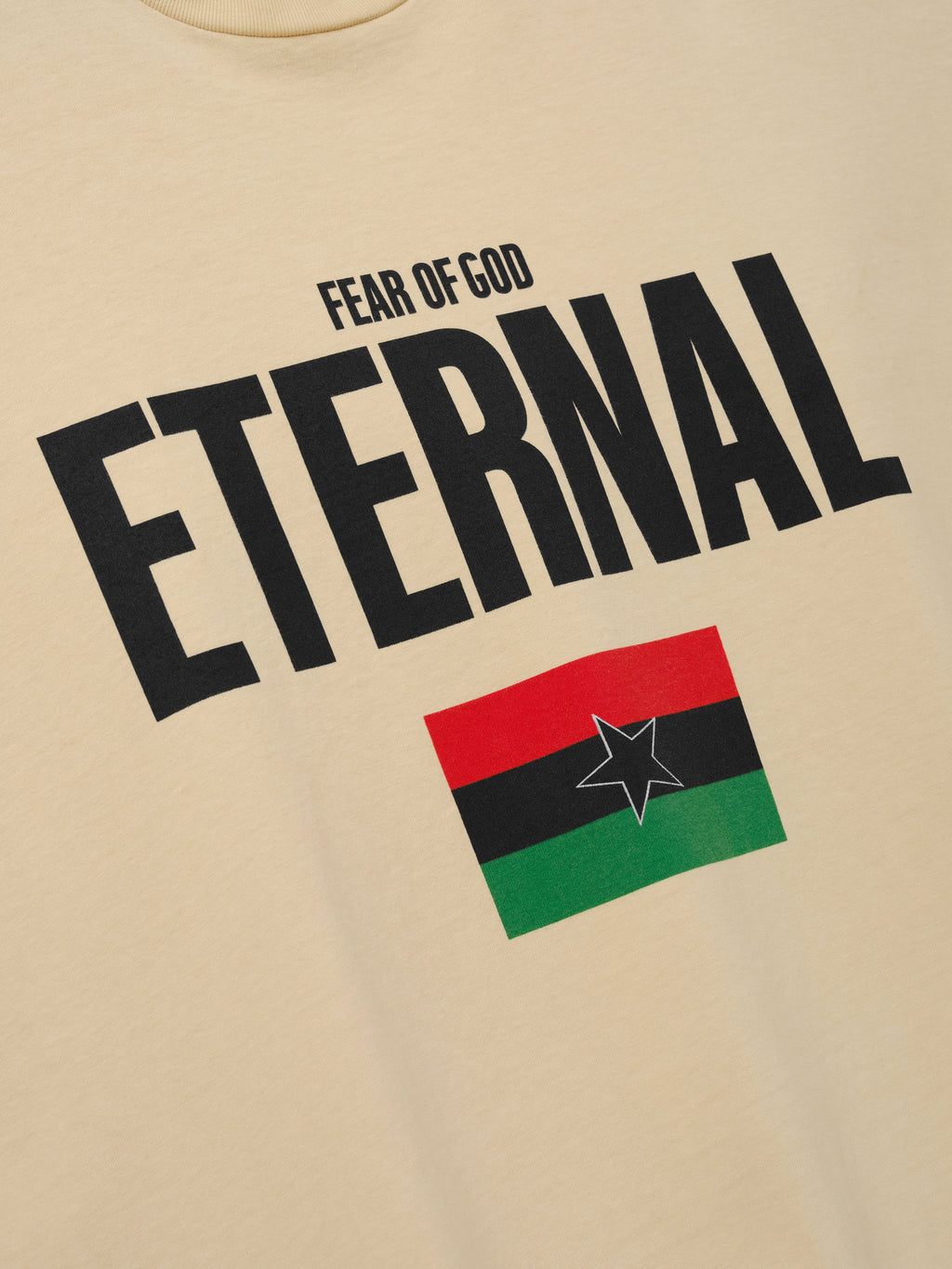 Reflection Eternal Tee in beige shown in close detail with bold black Fear of God Eternal lettering and red black green flag graphic with outlined star as Tops