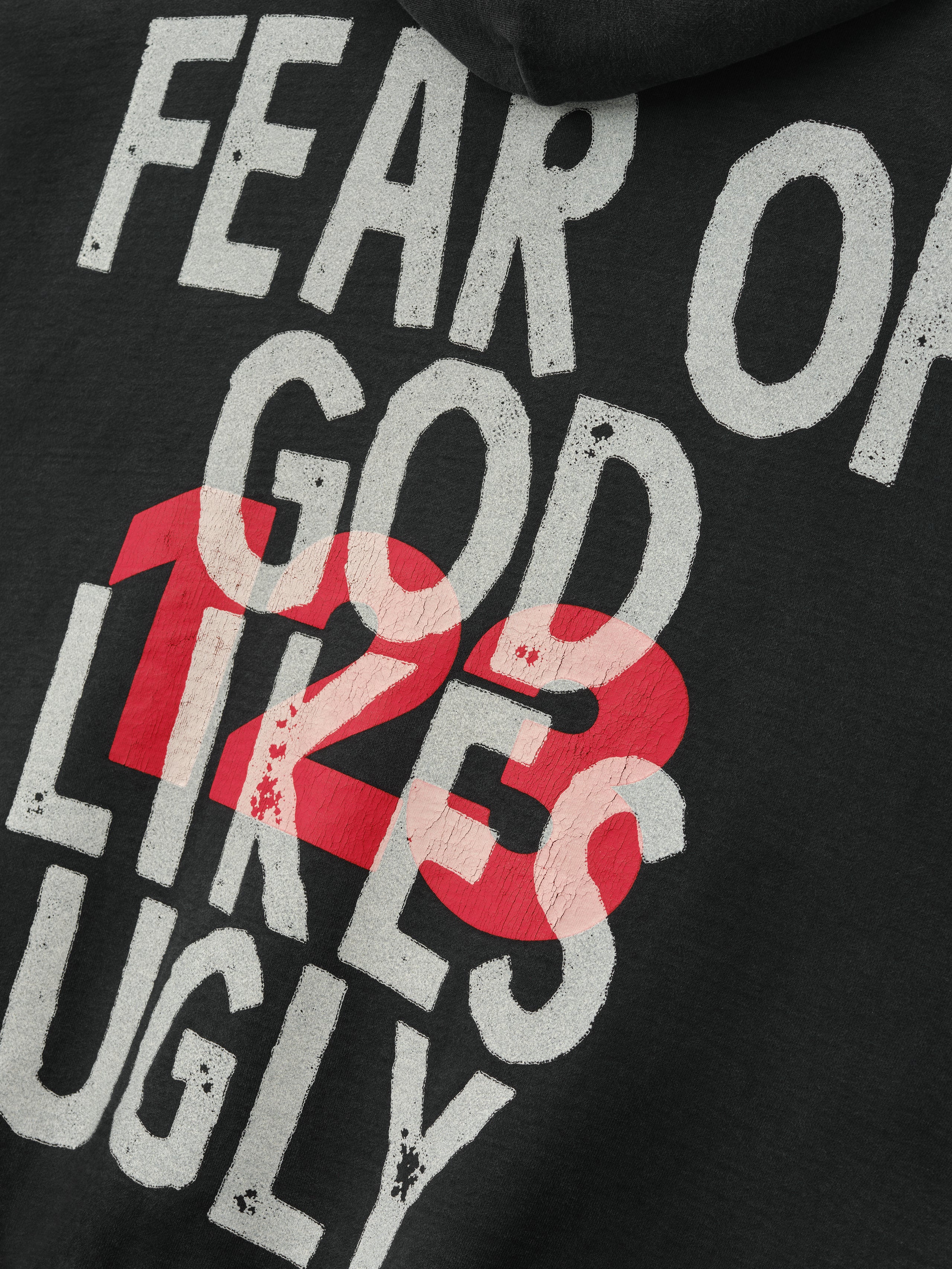 black hoodie close-up with distressed white Fear of God God Does Like Ugly text and red 12 overlay graphic